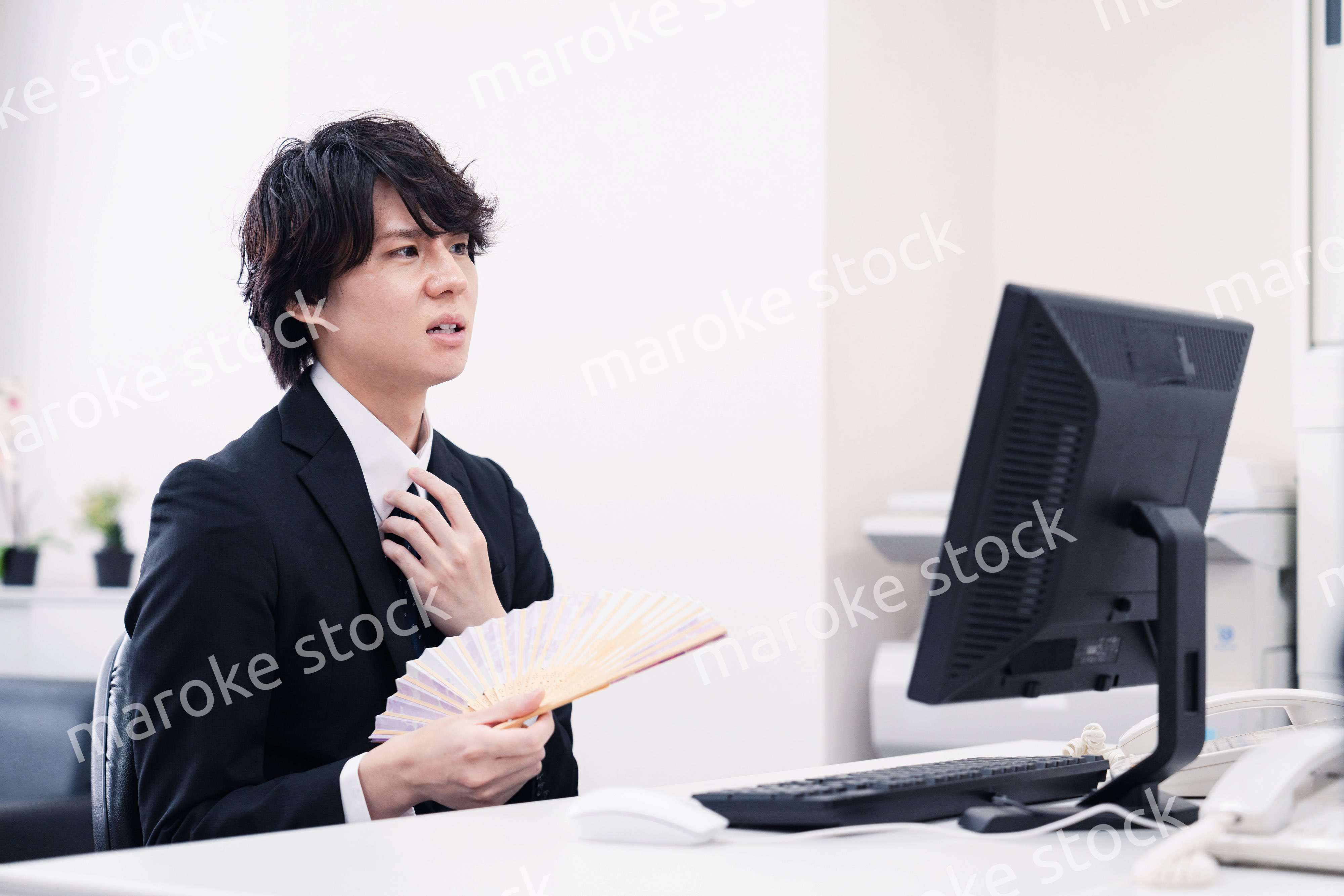 扇子で扇ぎながら仕事をするビジネスマン