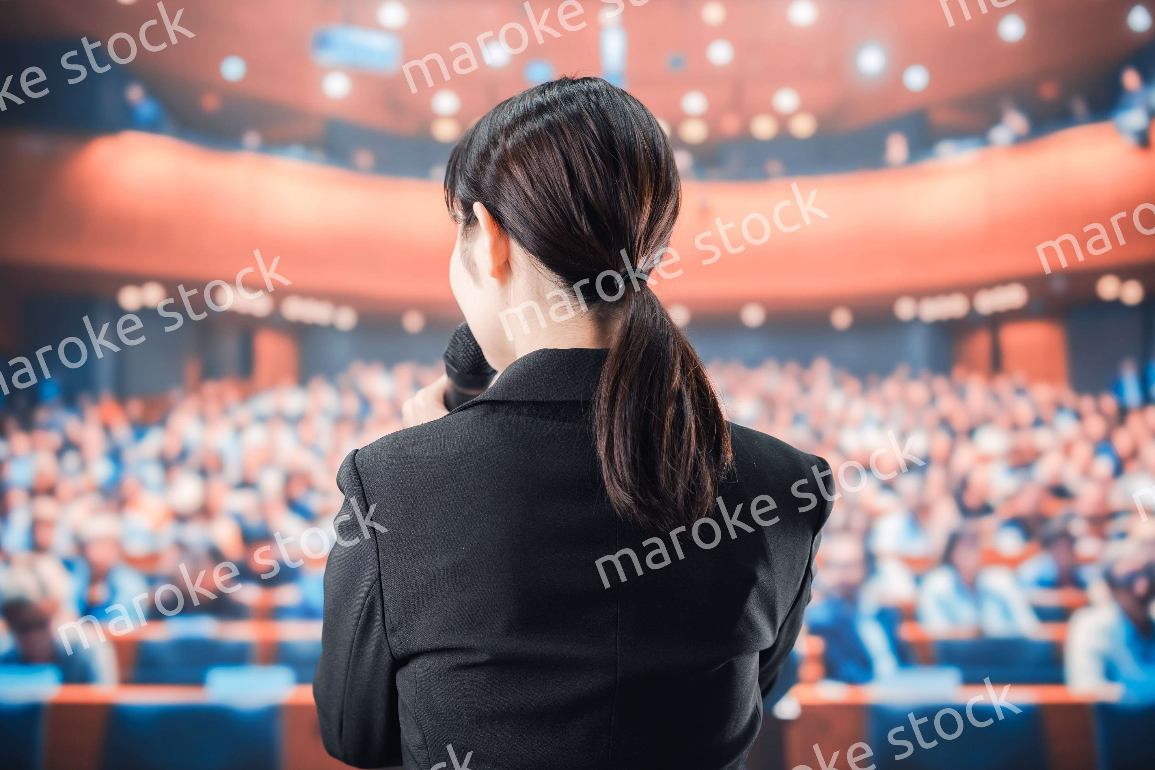 大勢の前でマイクで話す女性