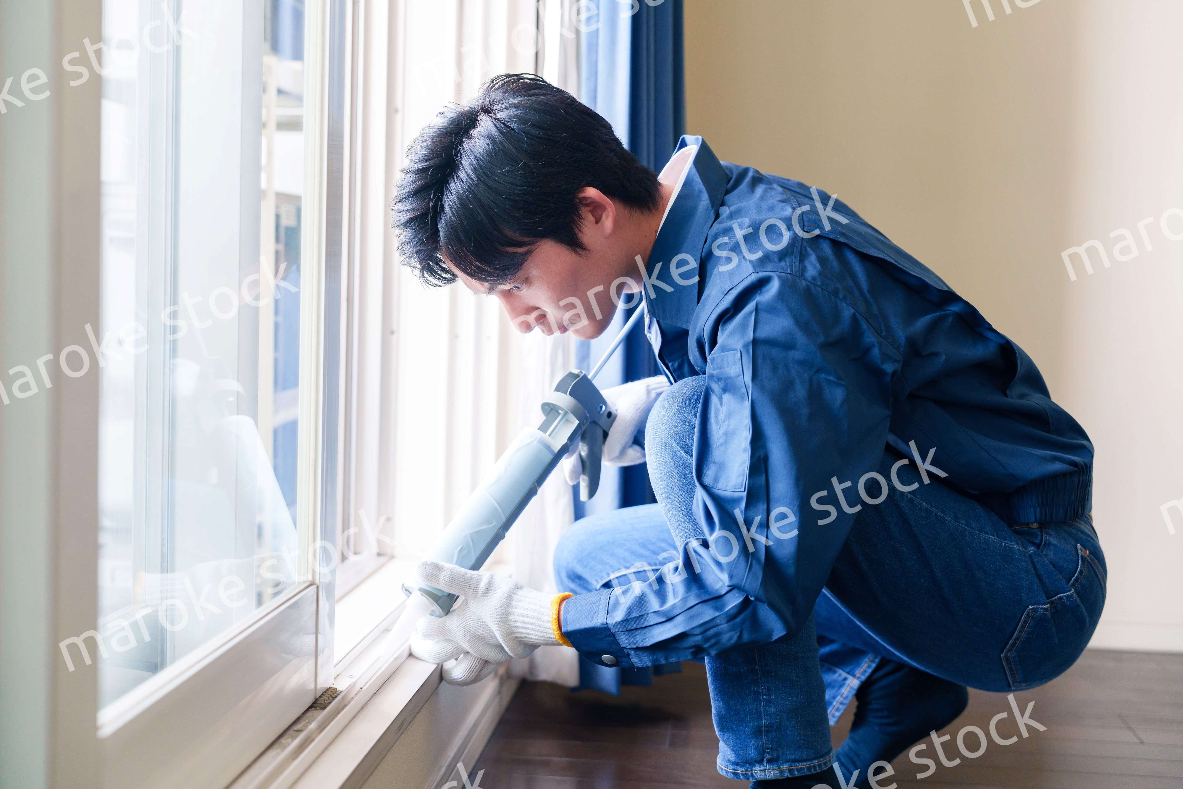 窓にコーキング材を塗る男性の作業員