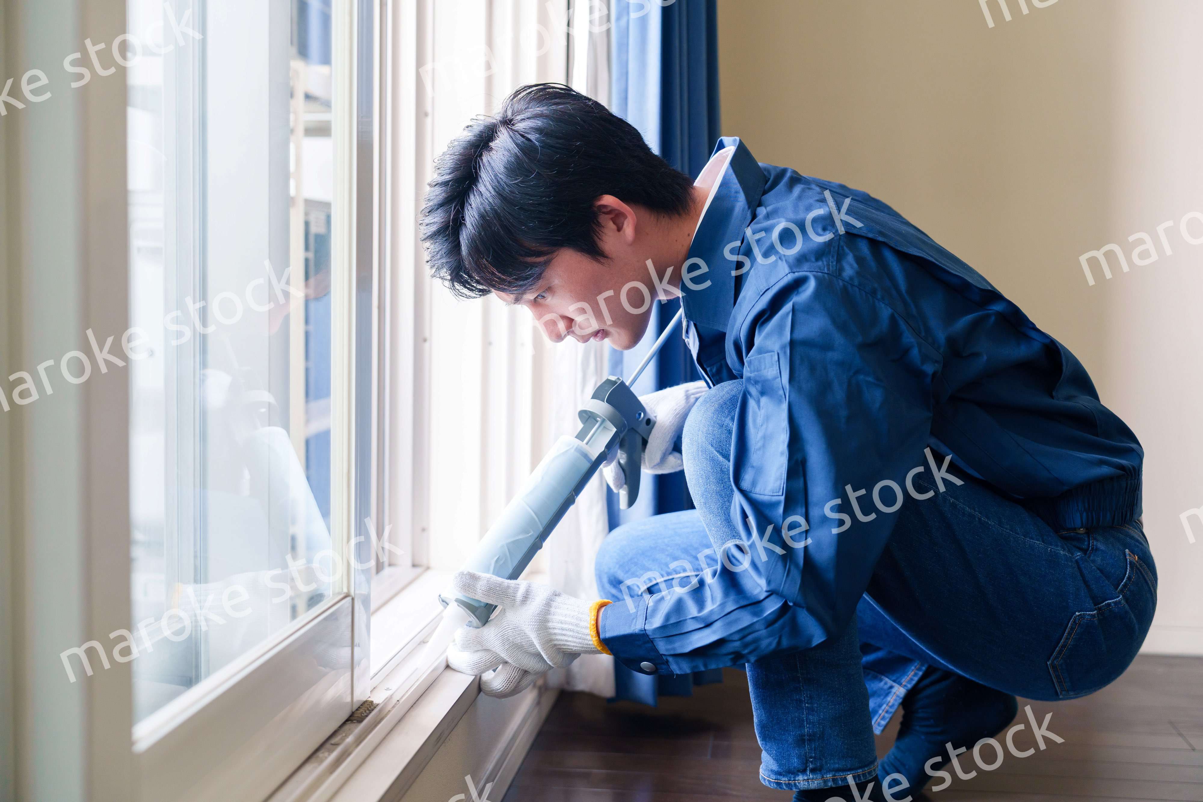 窓にコーキング材を塗る男性の作業員
