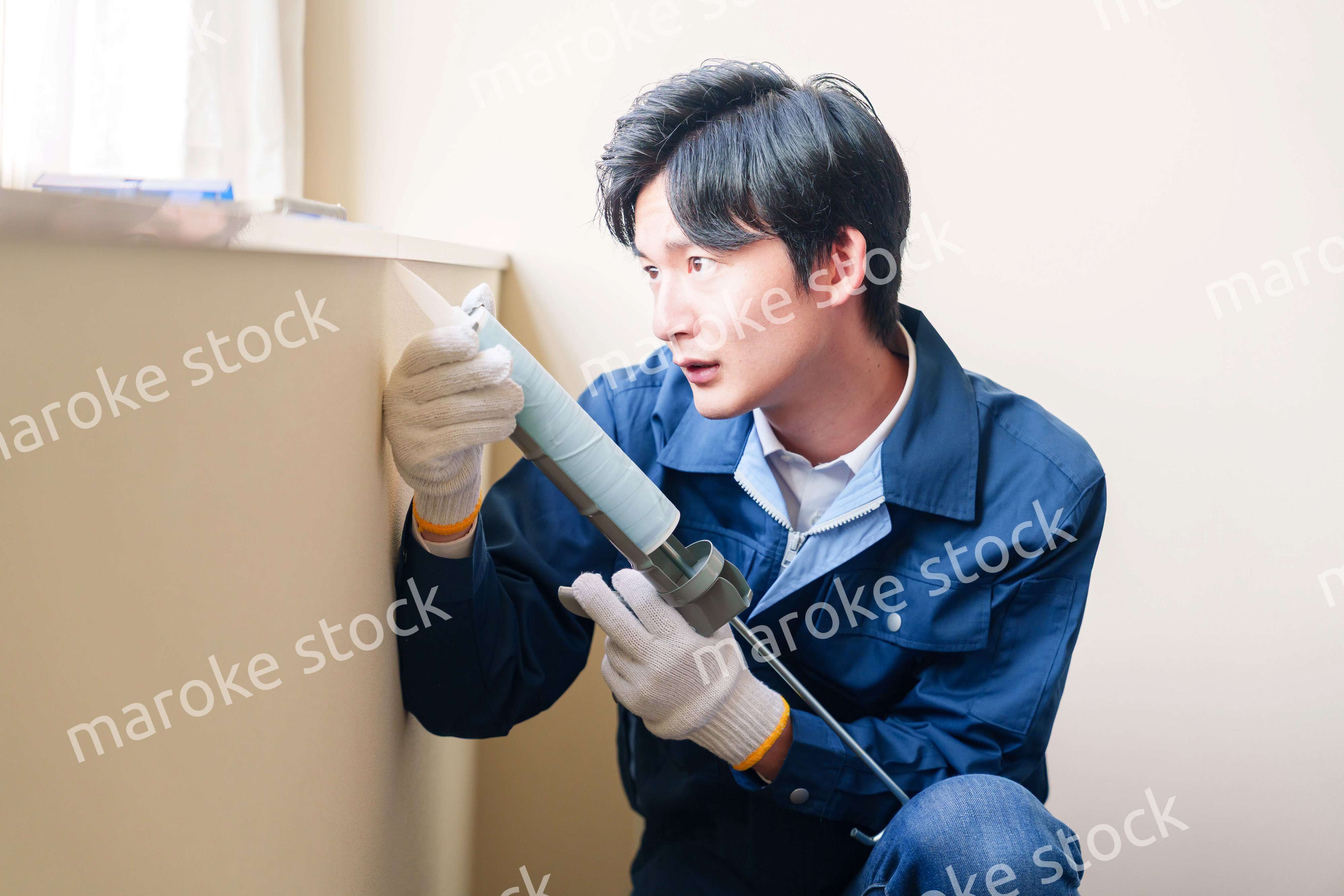 窓にコーキング材を塗る男性の作業員