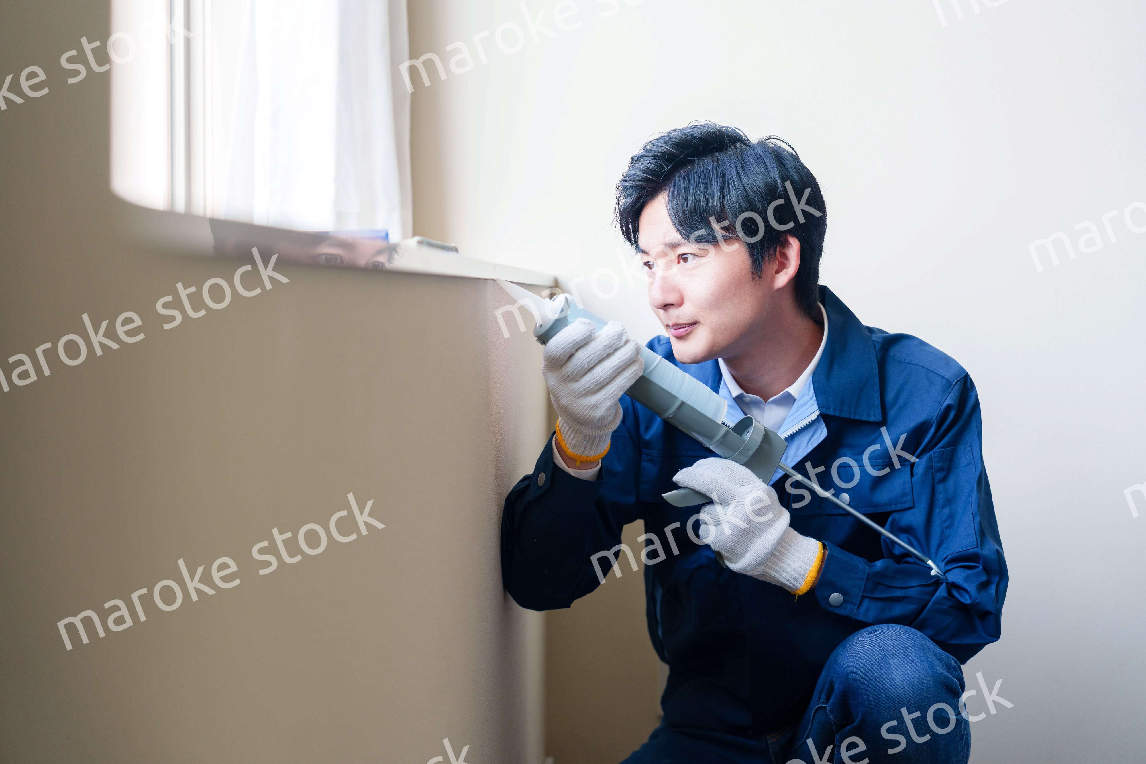 窓にコーキング材を塗る男性の作業員