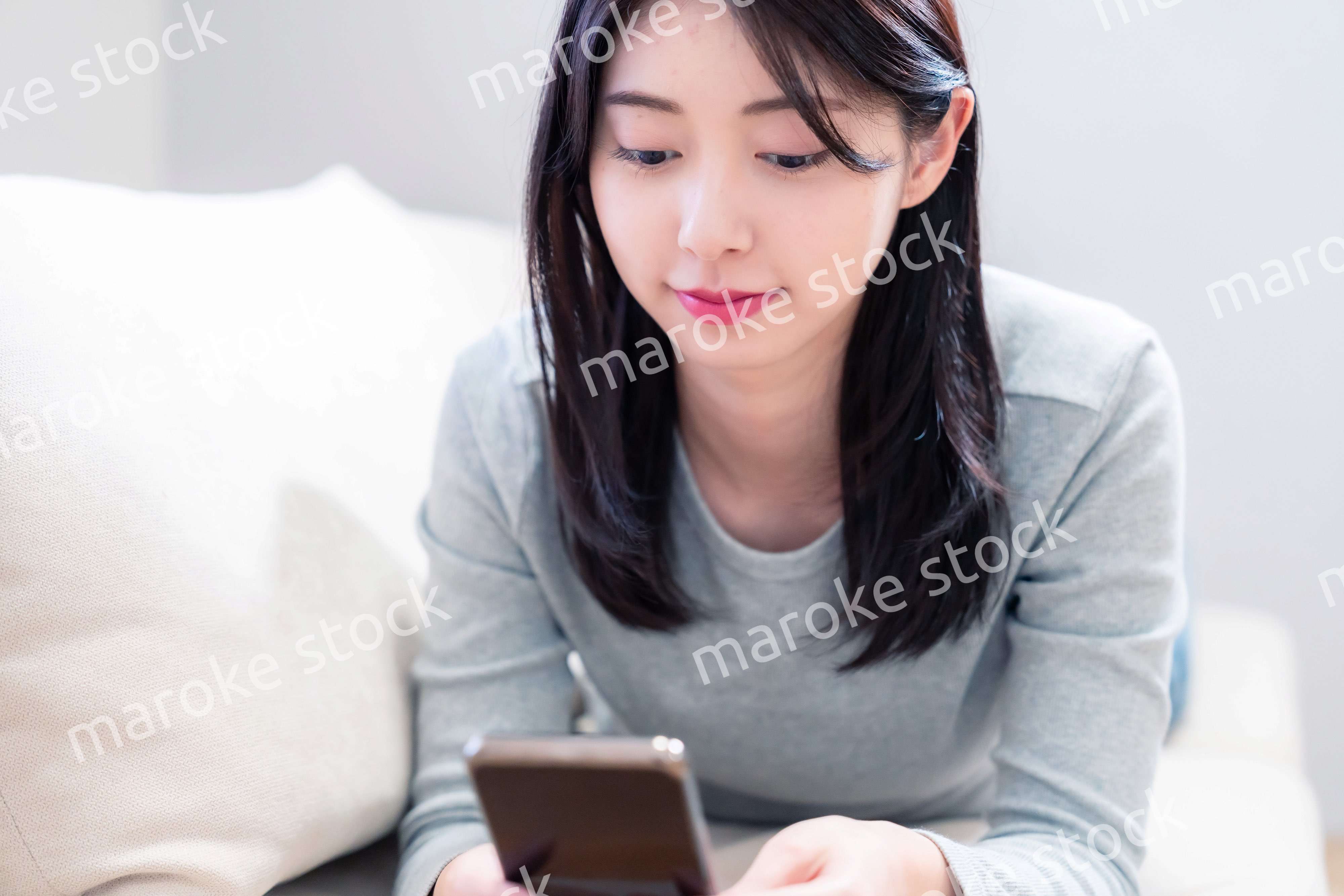 ソファでリラックスをしてスマホを使う若い女性