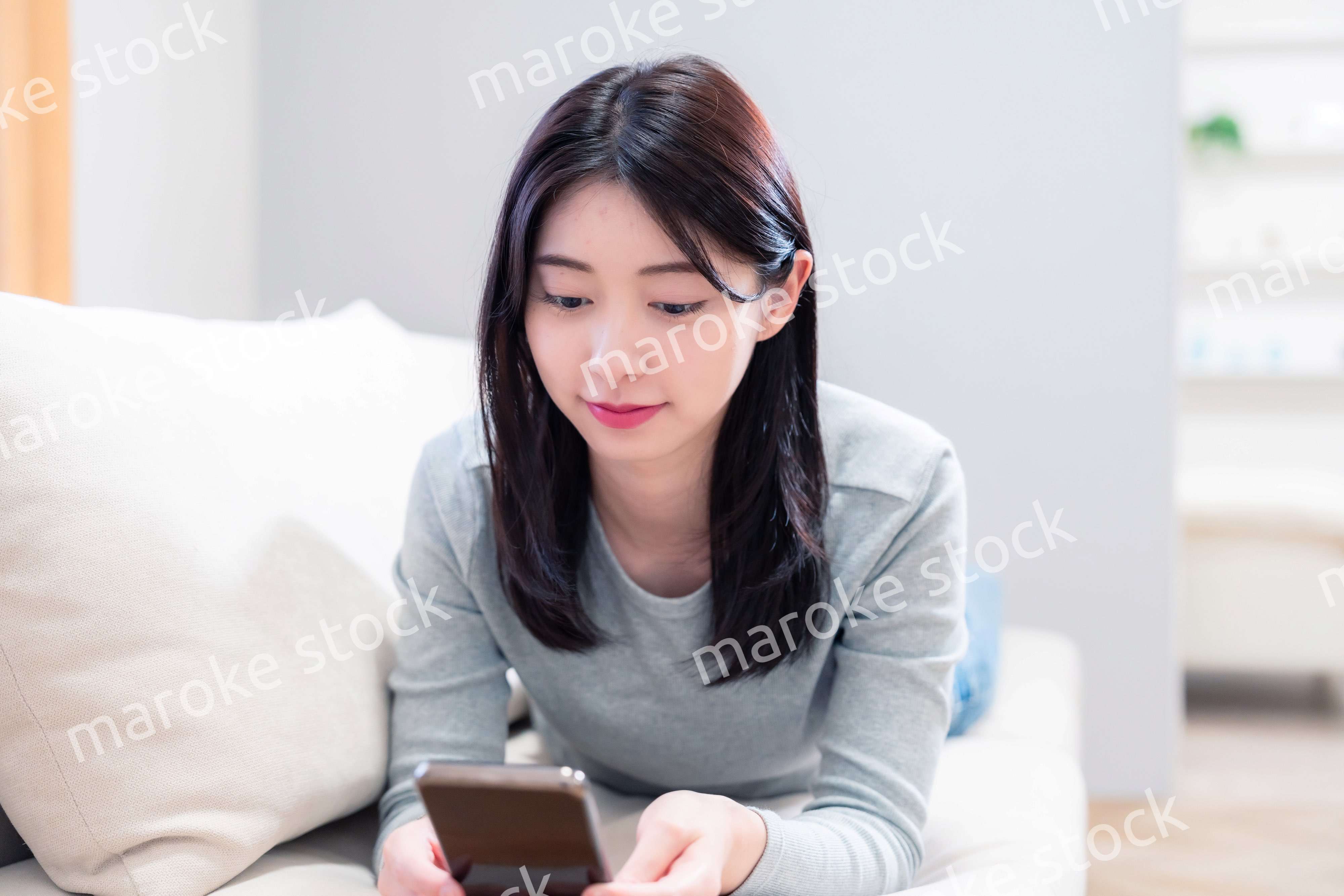 ソファでリラックスをしてスマホを使う若い女性