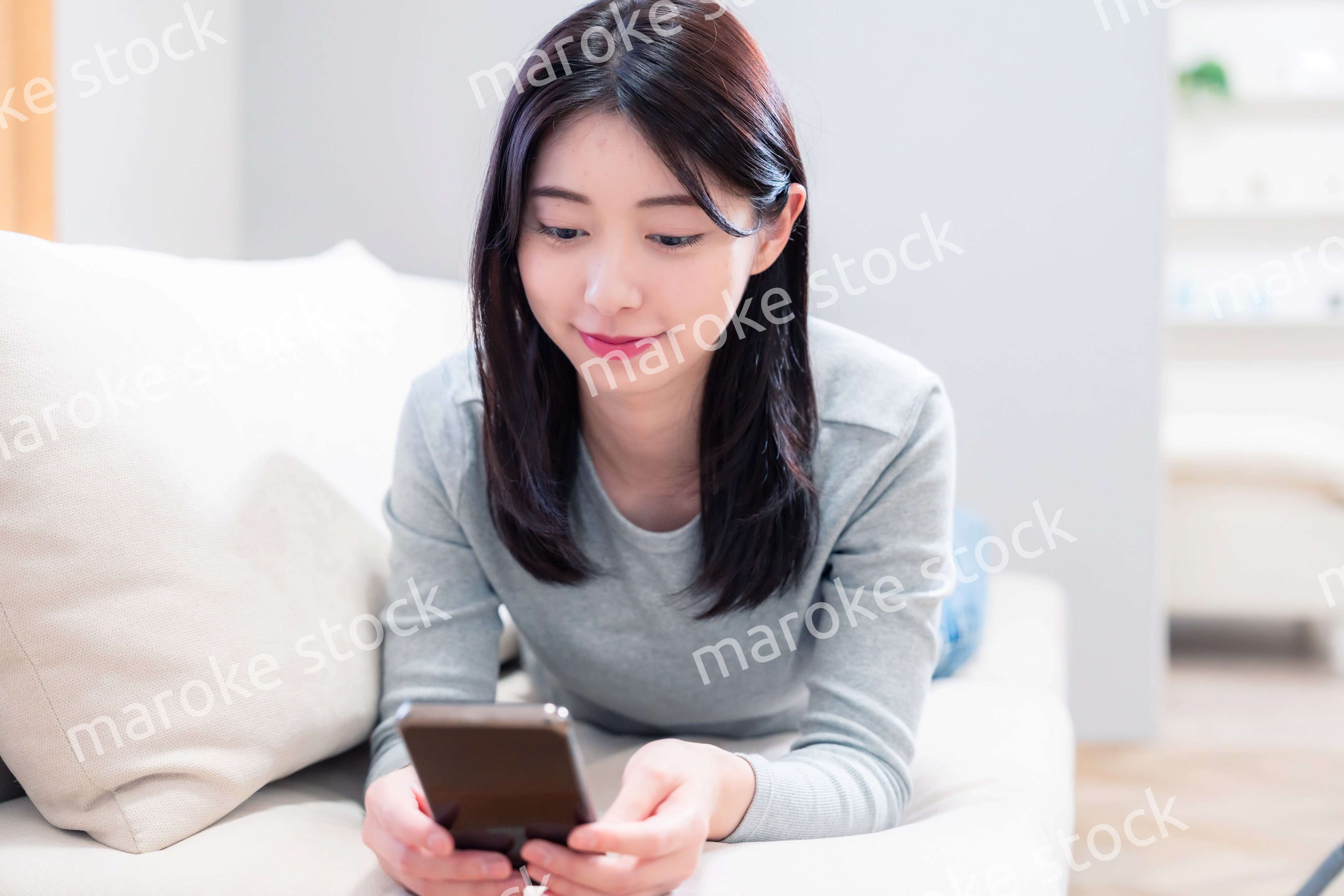 ソファでリラックスをしてスマホを使う若い女性