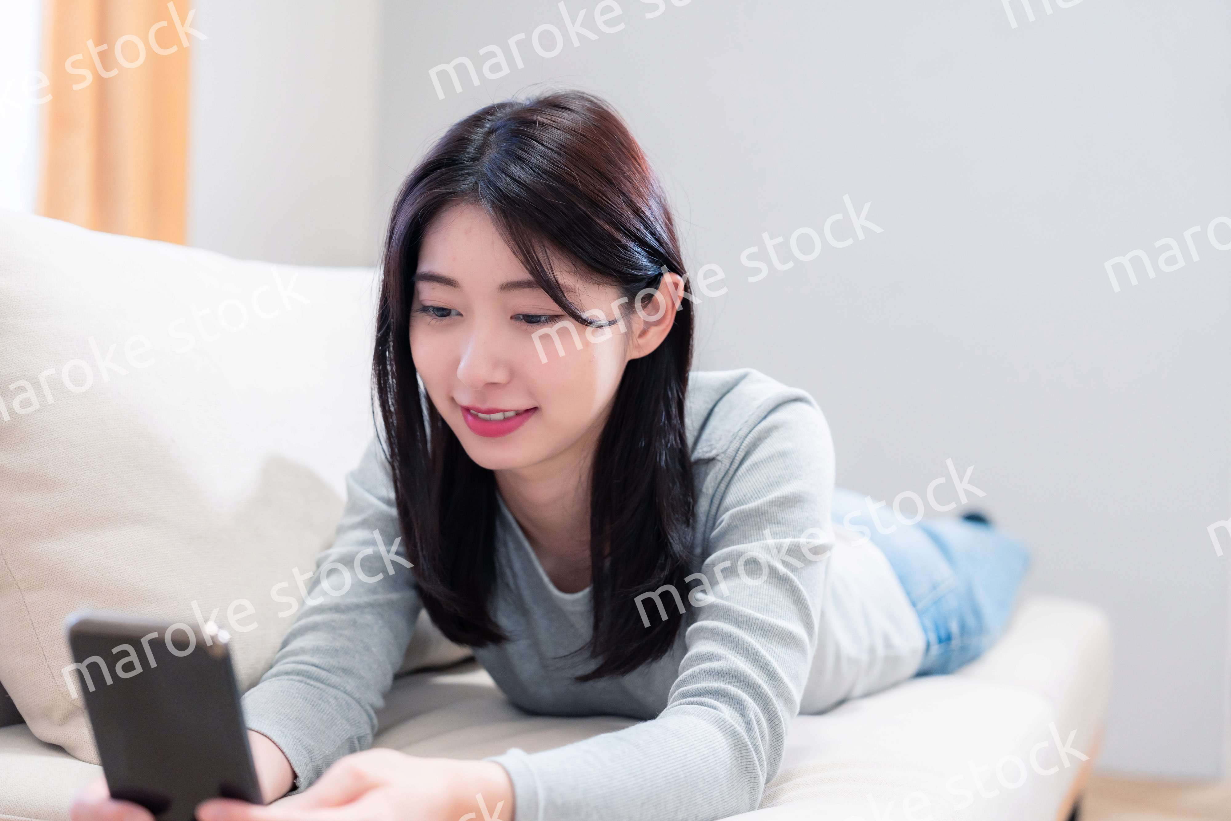 ソファでリラックスをしてスマホを使う若い女性