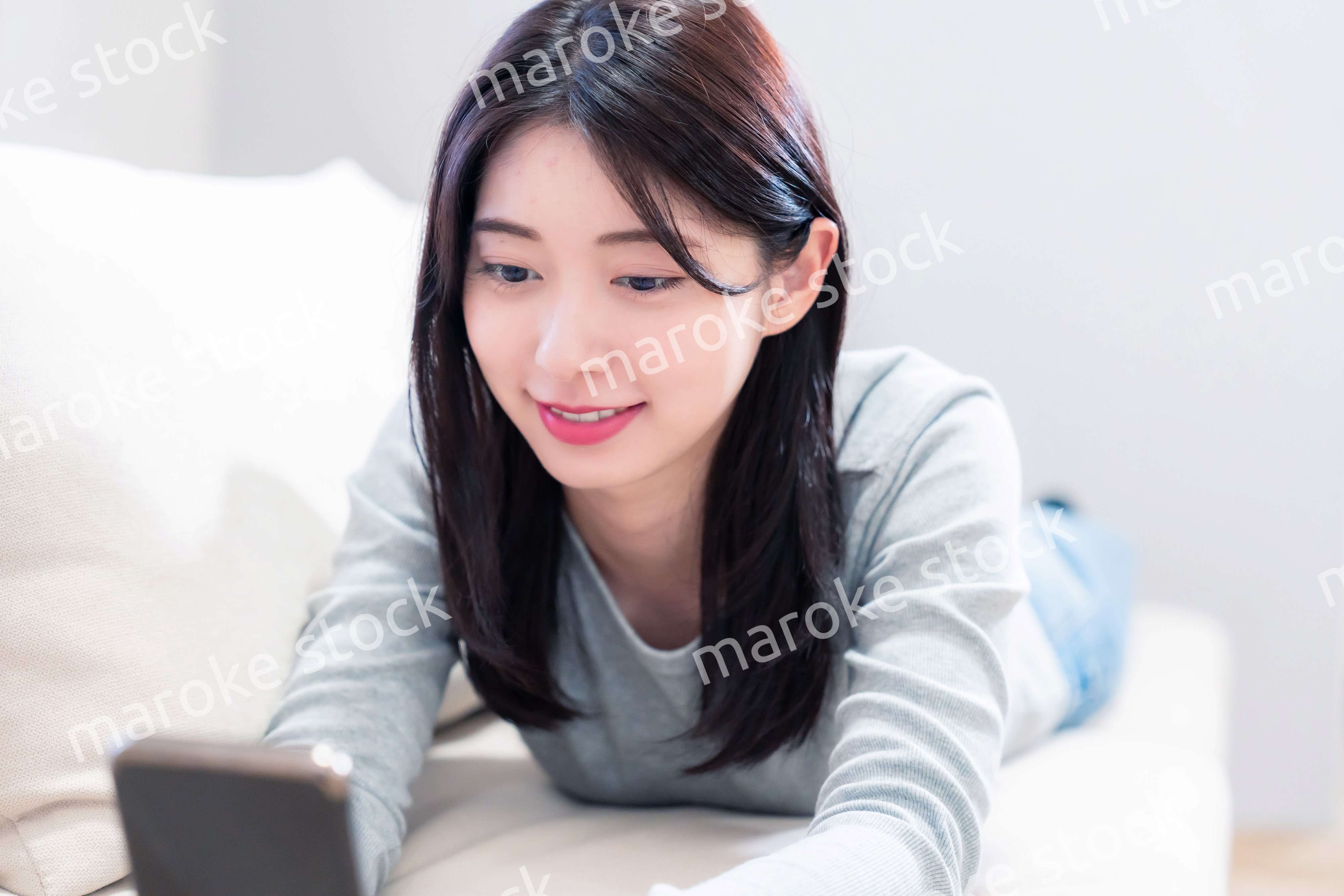 ソファでリラックスをしてスマホを使う若い女性