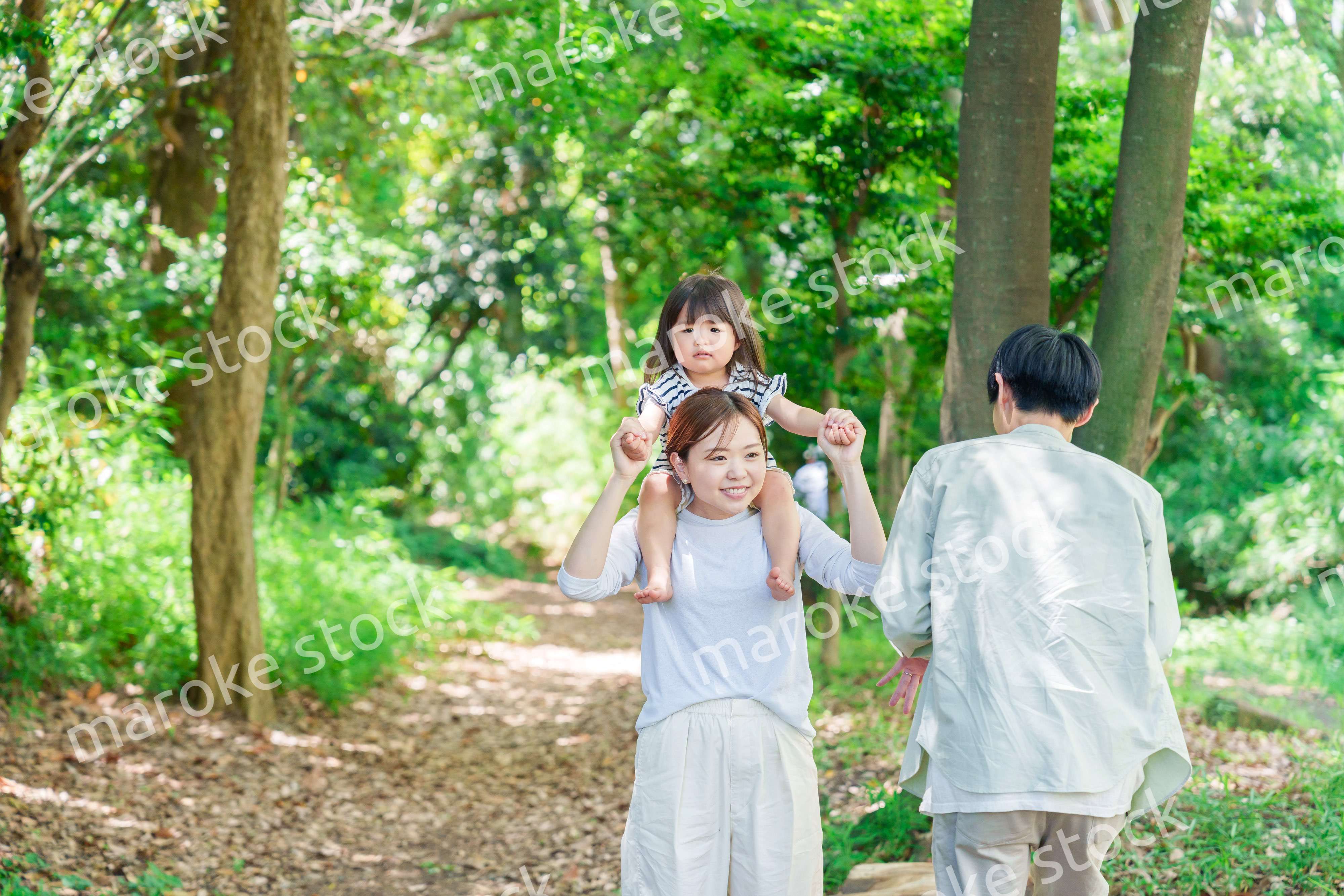 子どもを肩車して森の中を歩く家族