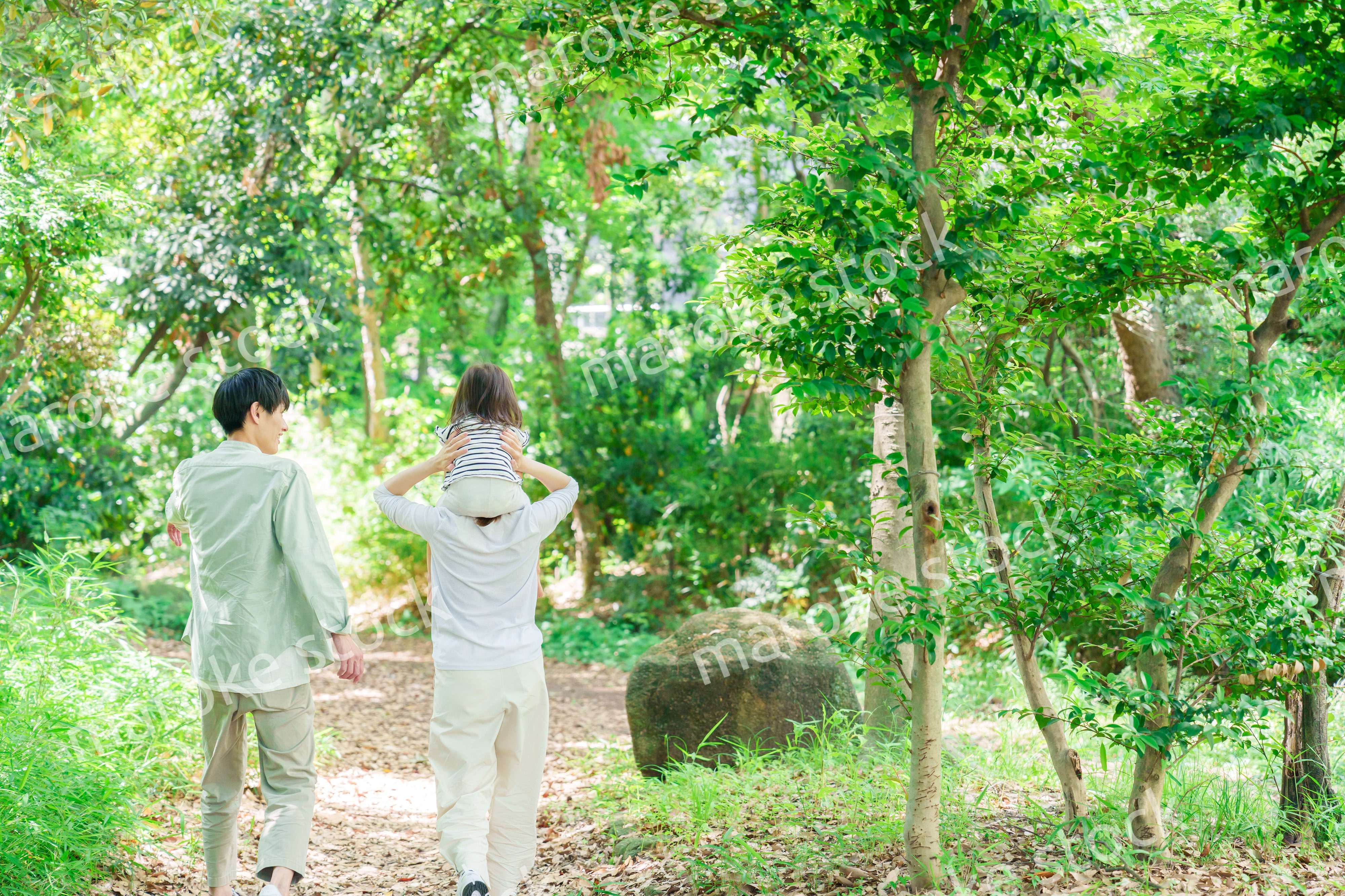 子どもを肩車して森の中を歩く家族