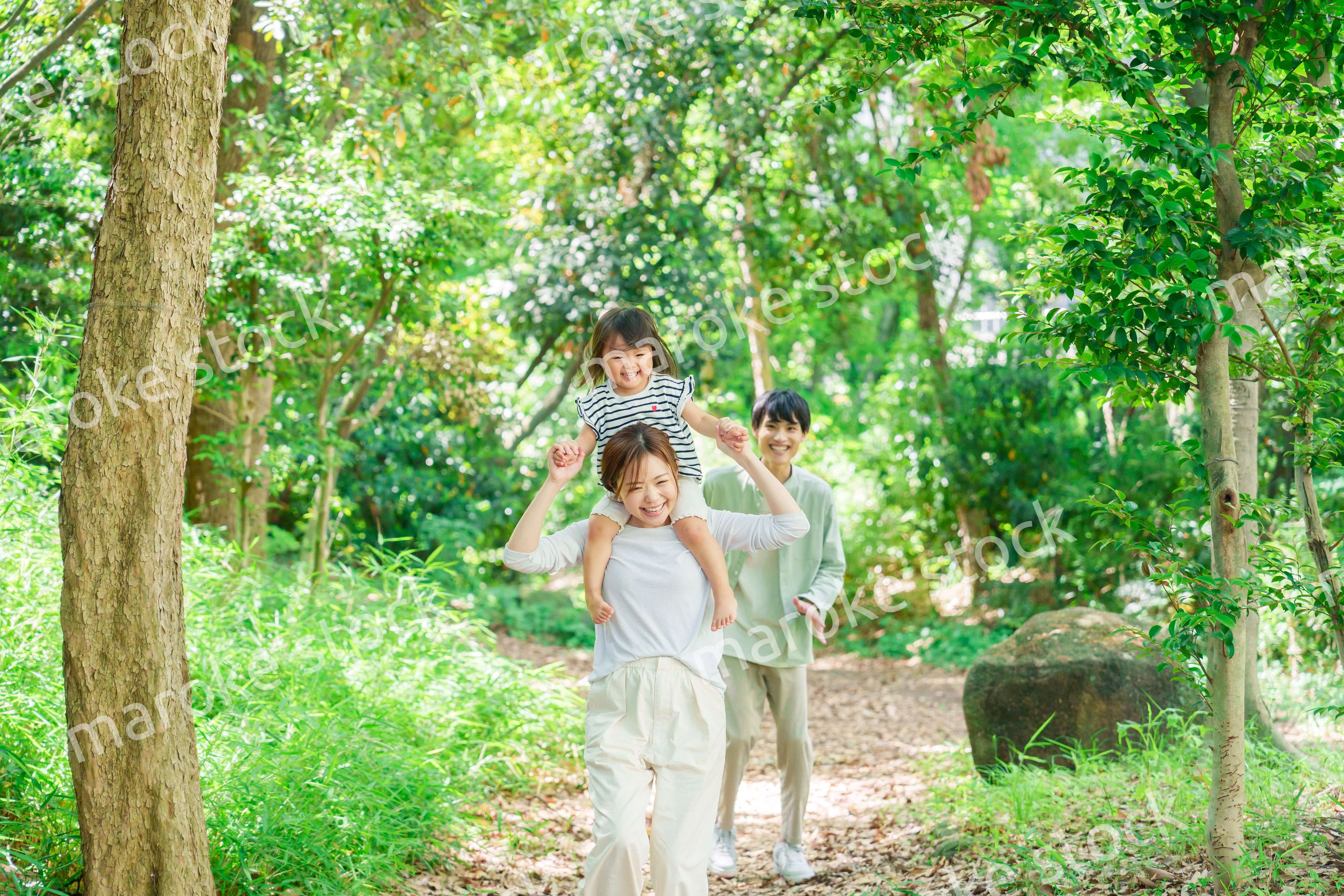 子どもを肩車して森の中を歩く家族