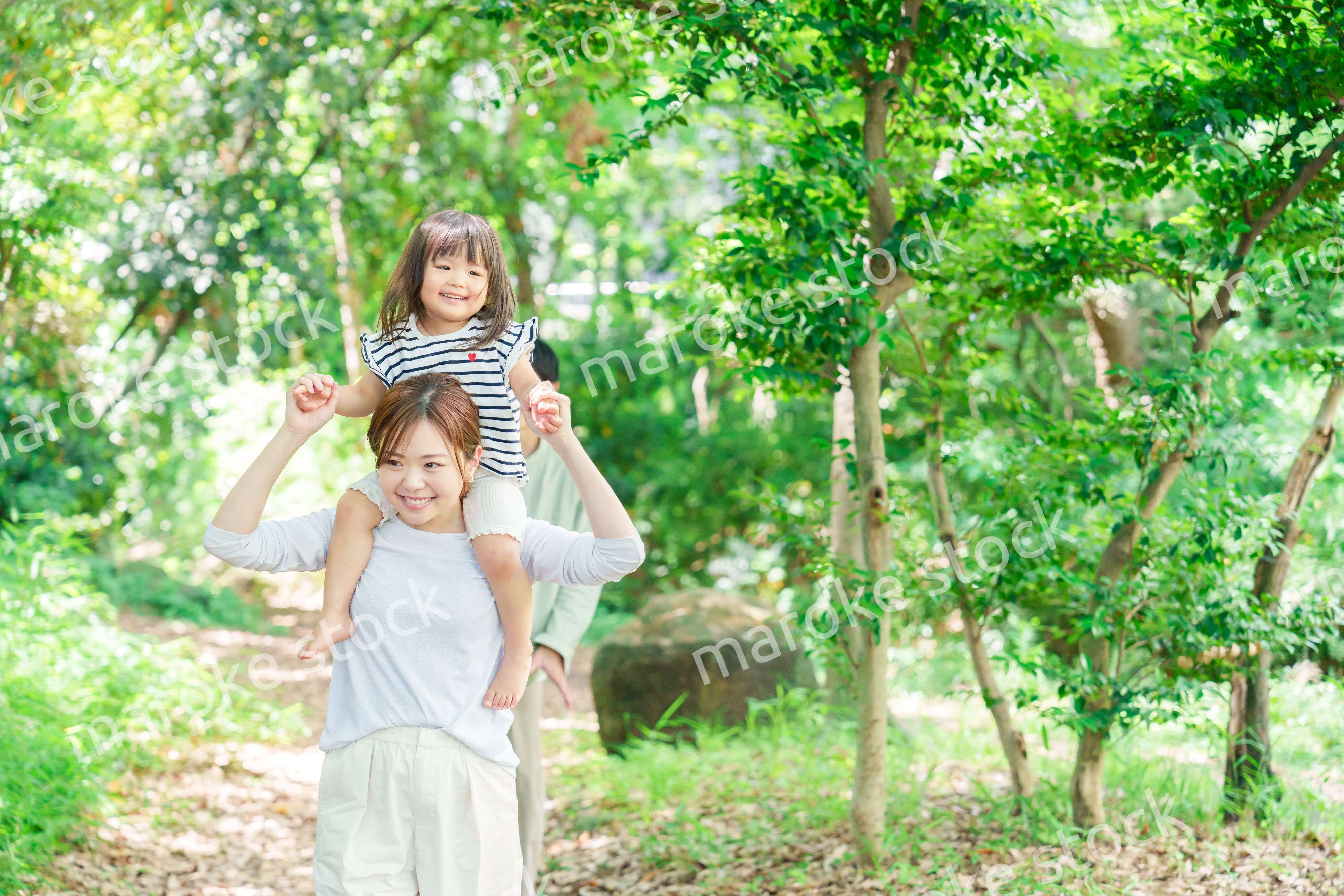 子どもを肩車して森の中を歩く家族