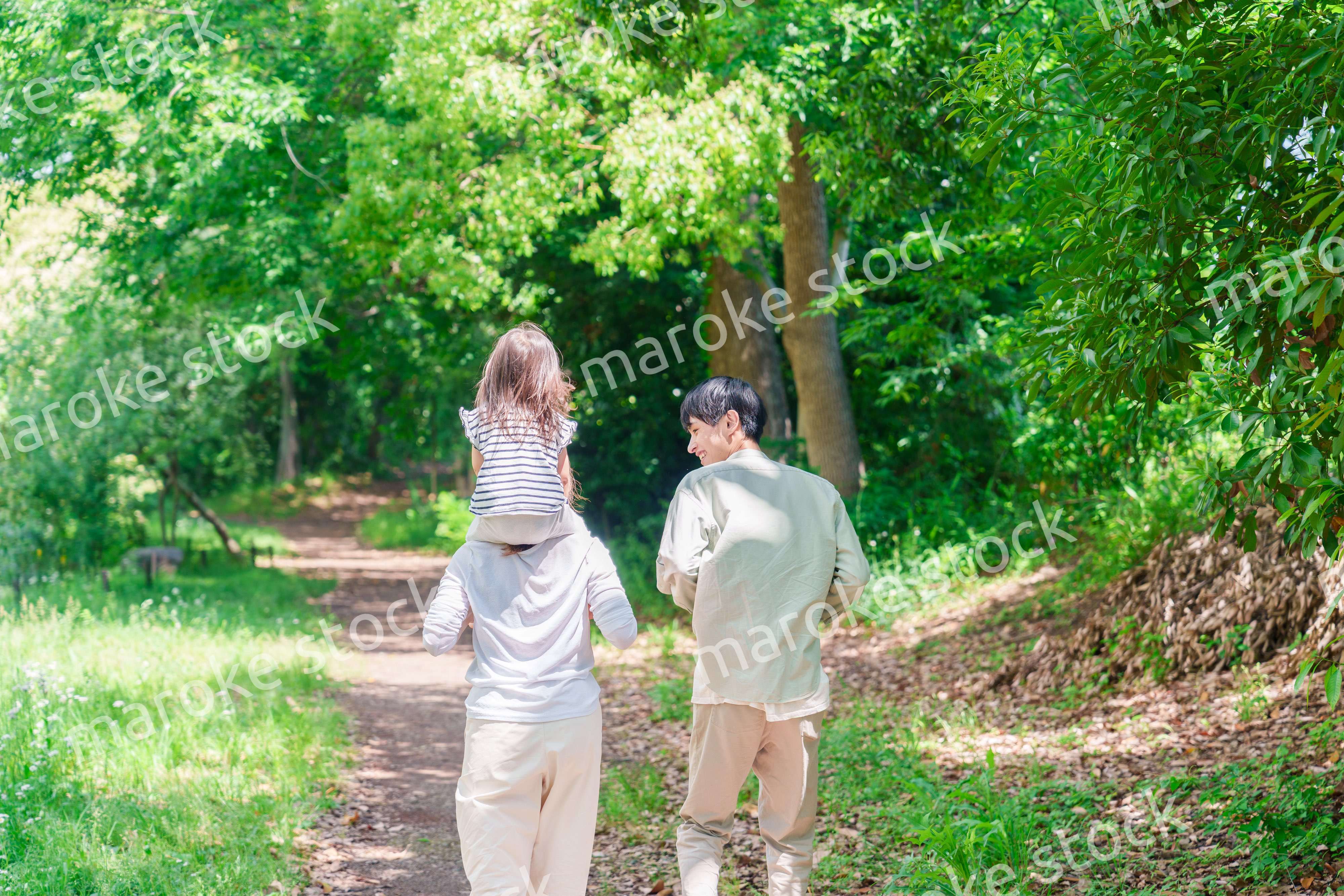 子どもを肩車して森の中を歩く家族