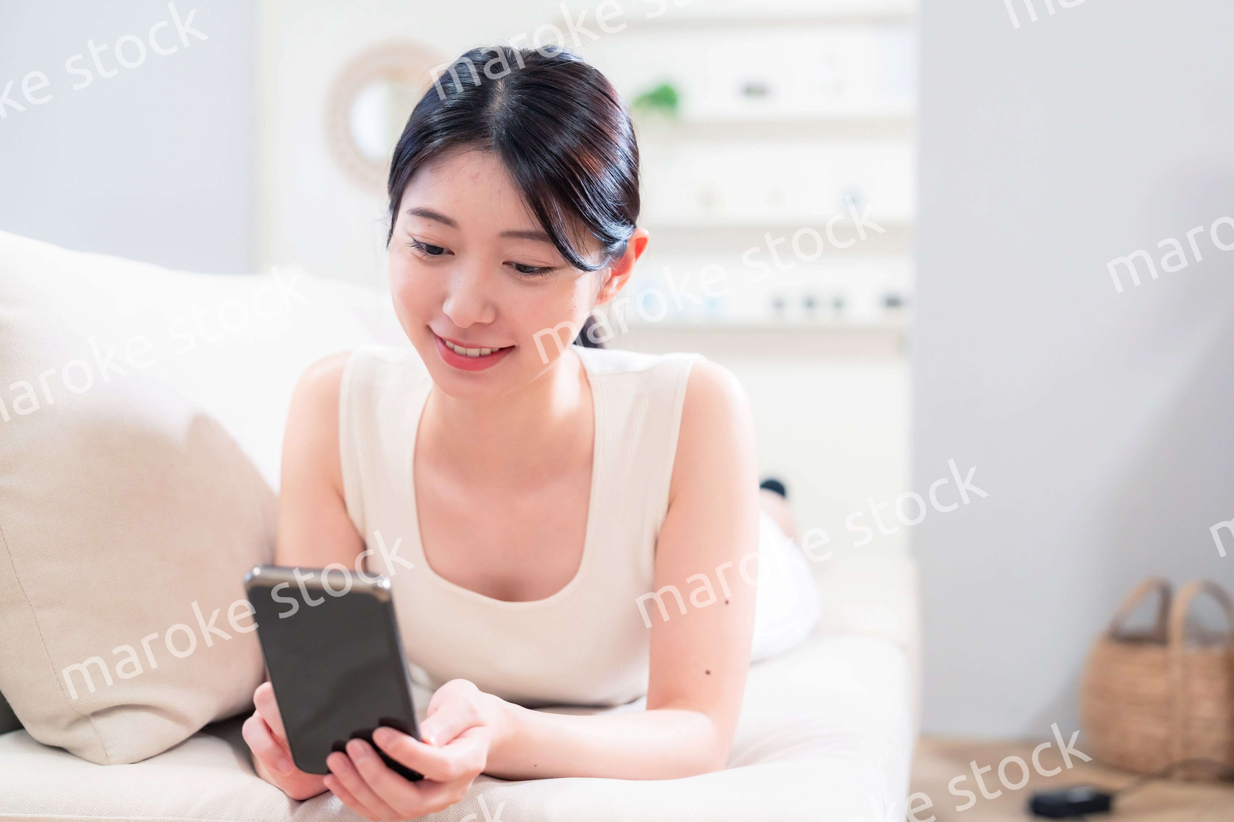 ソファで寝転がってスマホを使う若い女性