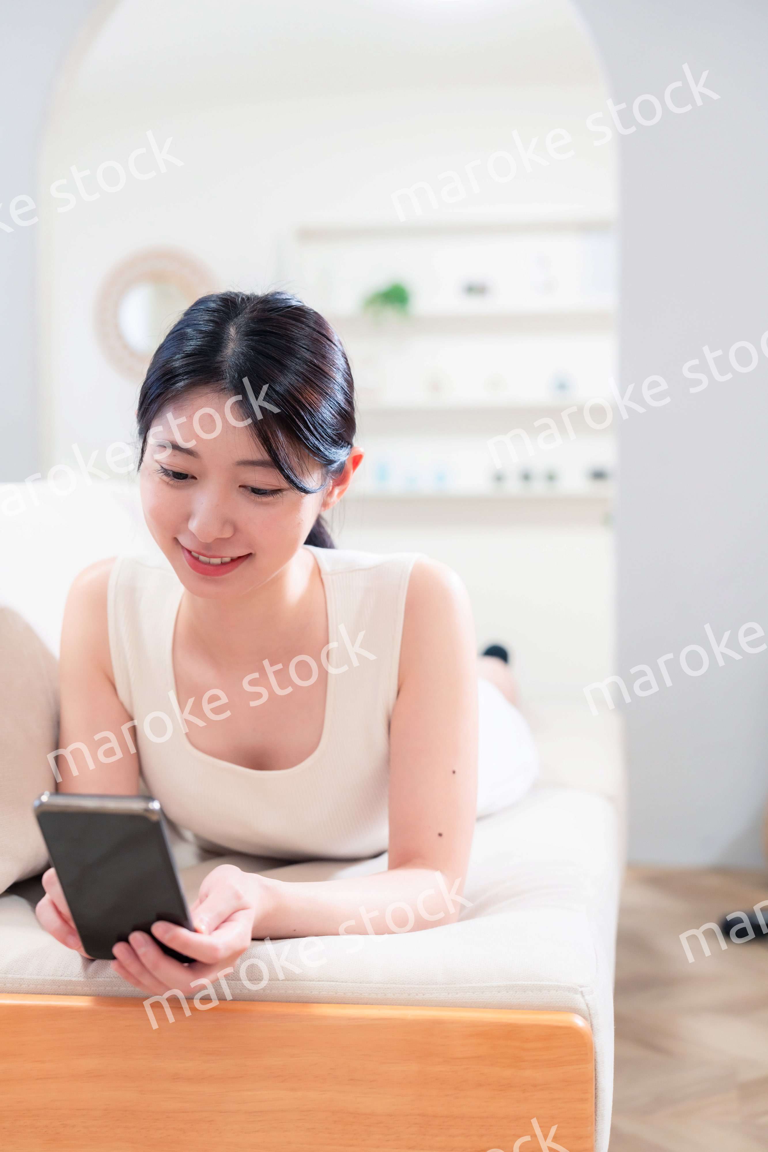 ソファで寝転がってスマホを使う若い女性