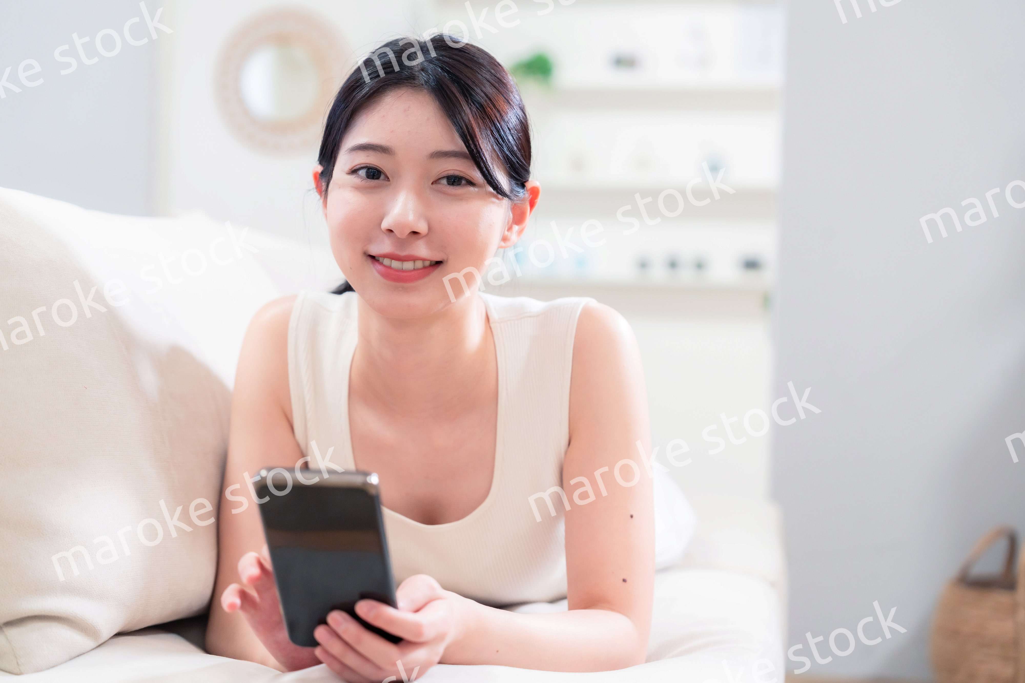 ソファで寝転がってスマホを使う若い女性