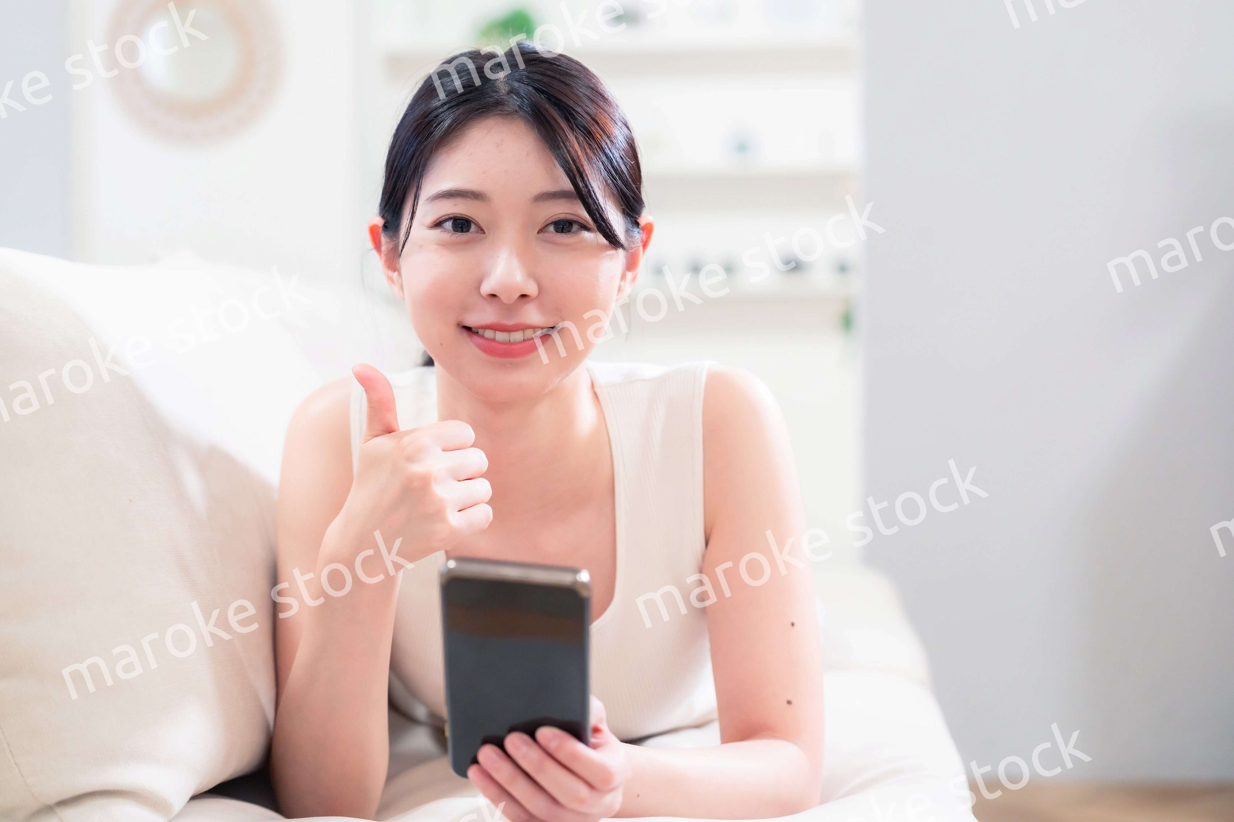 ソファで寝転がってスマホを使う若い女性