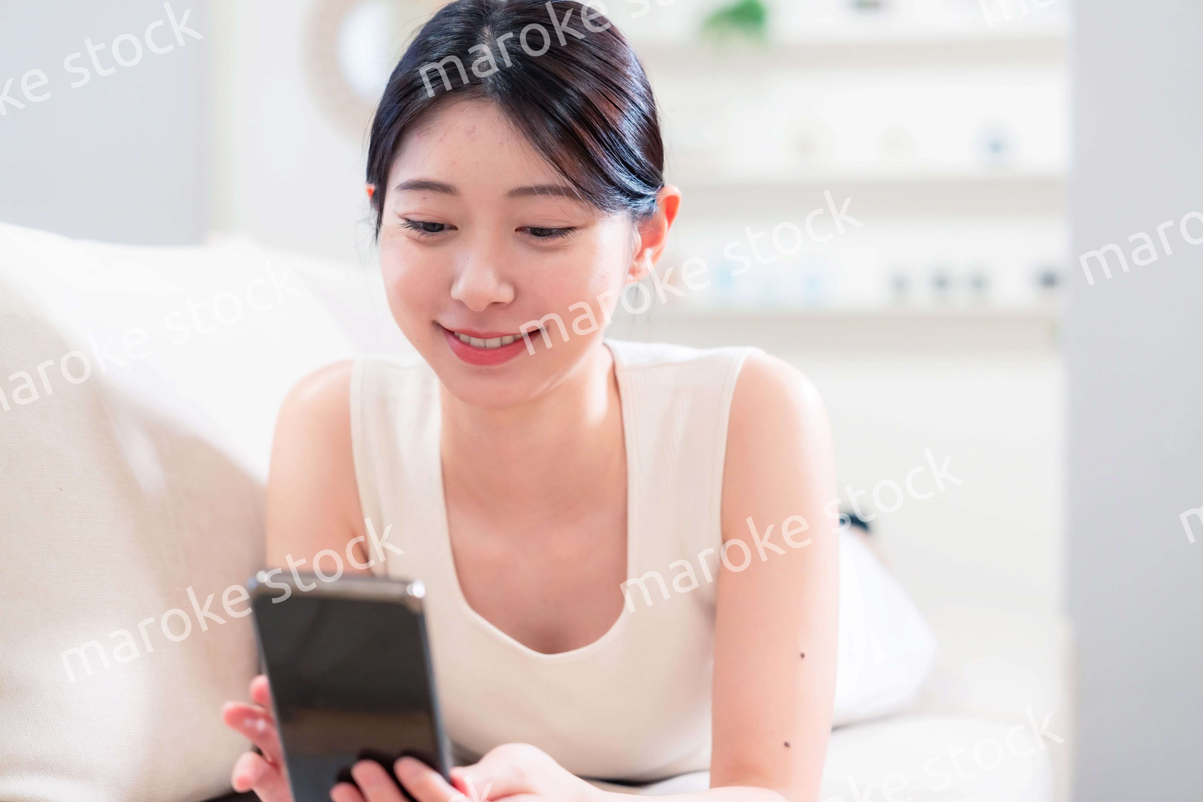 ソファで寝転がってスマホを使う若い女性