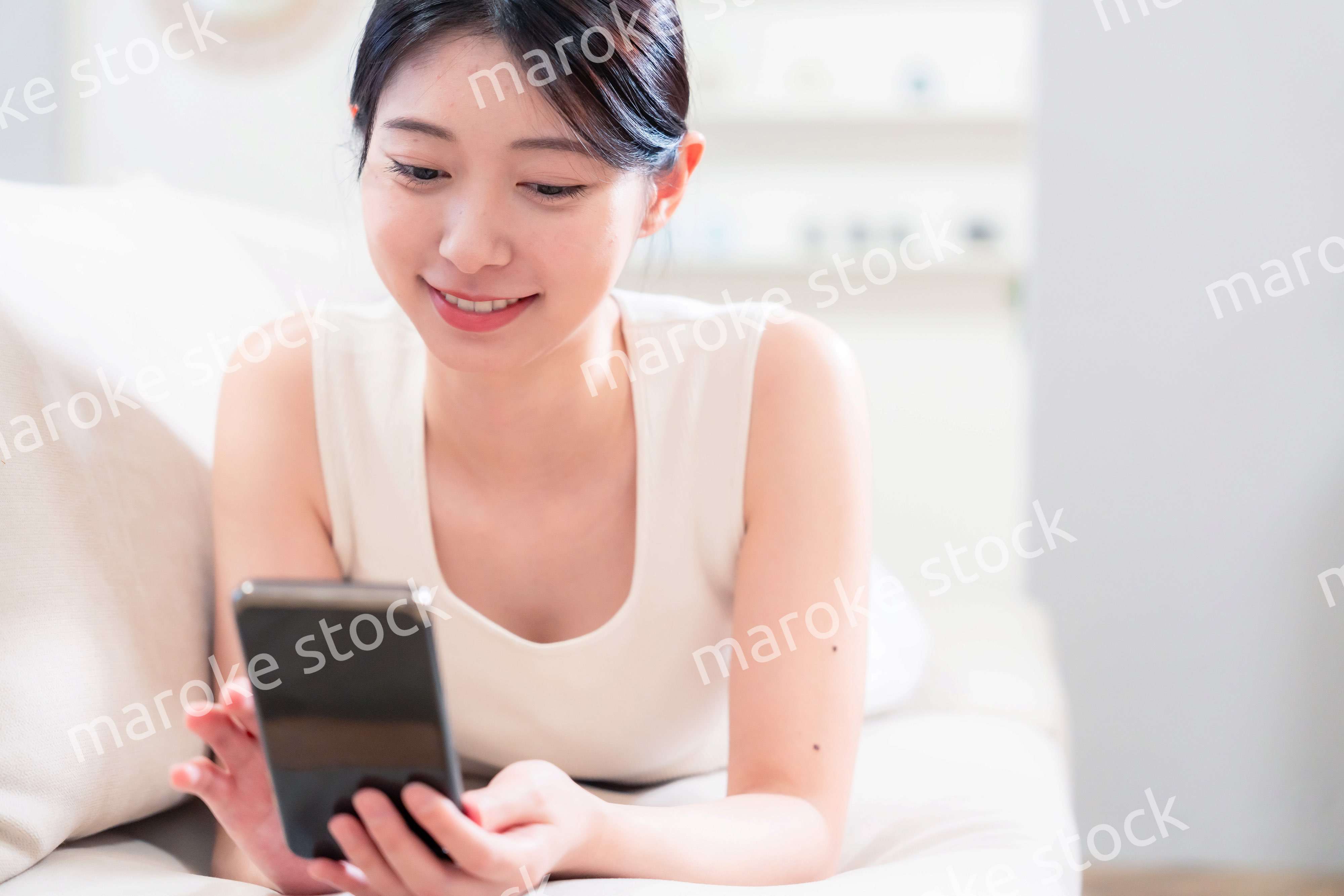 ソファで寝転がってスマホを使う若い女性