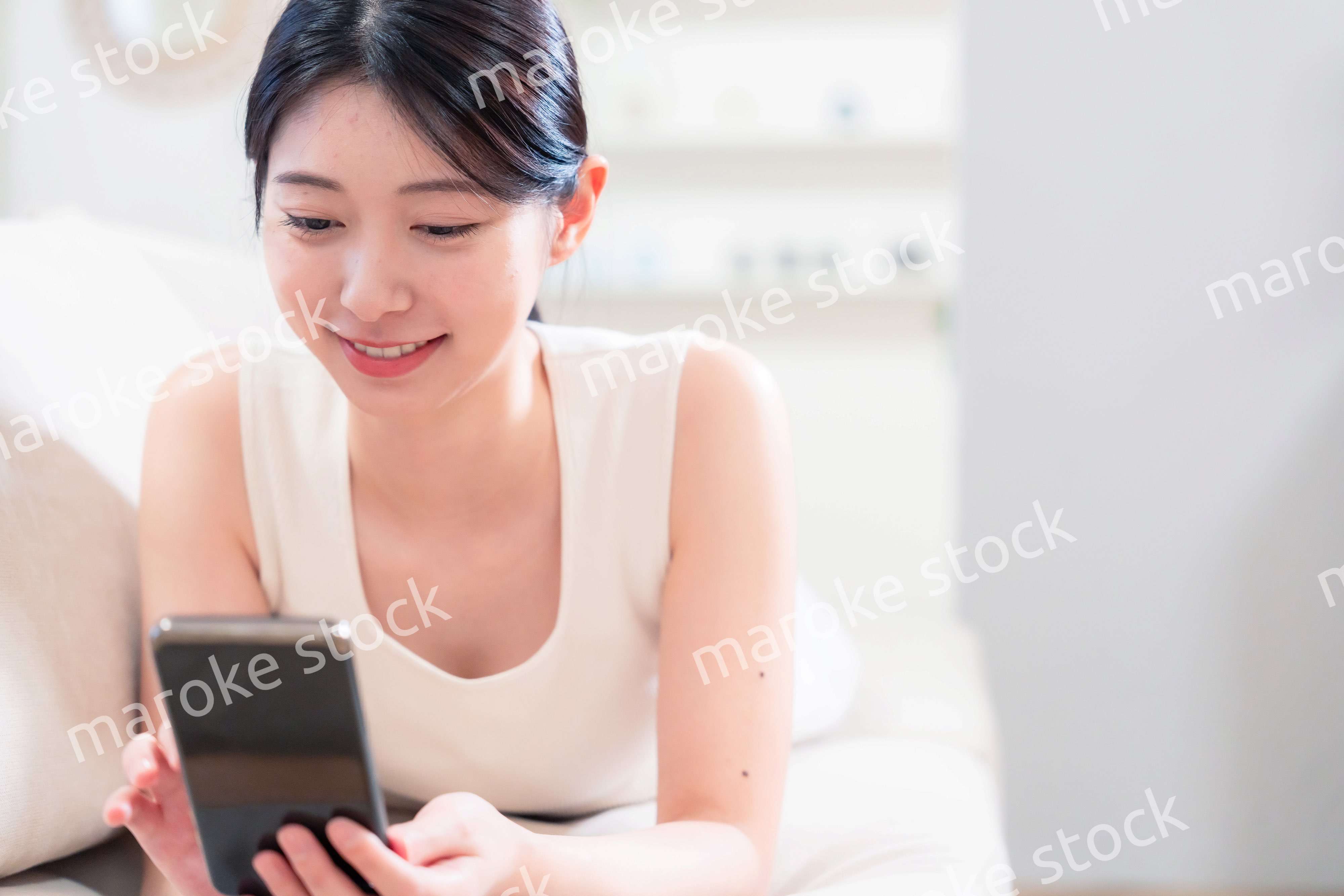 ソファで寝転がってスマホを使う若い女性