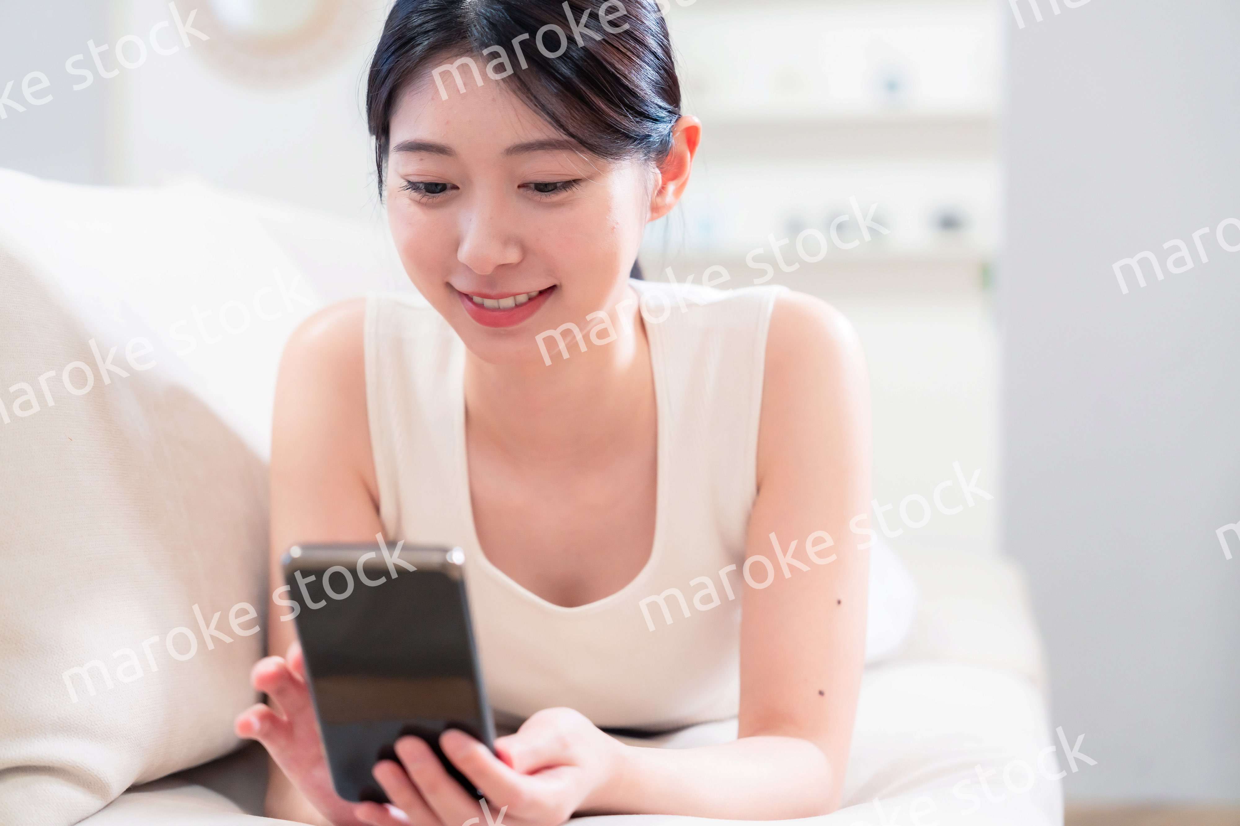 ソファで寝転がってスマホを使う若い女性