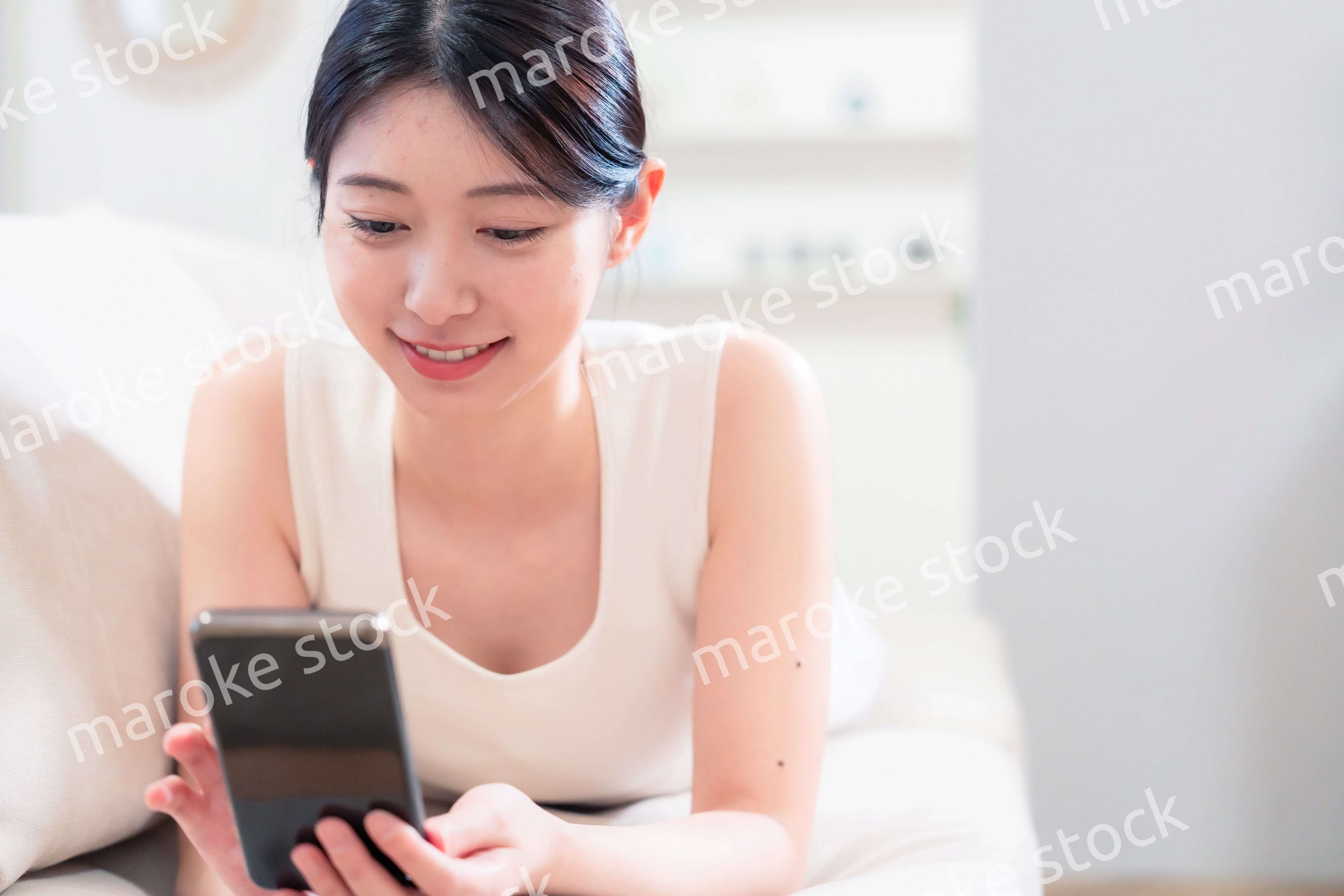 ソファで寝転がってスマホを使う若い女性