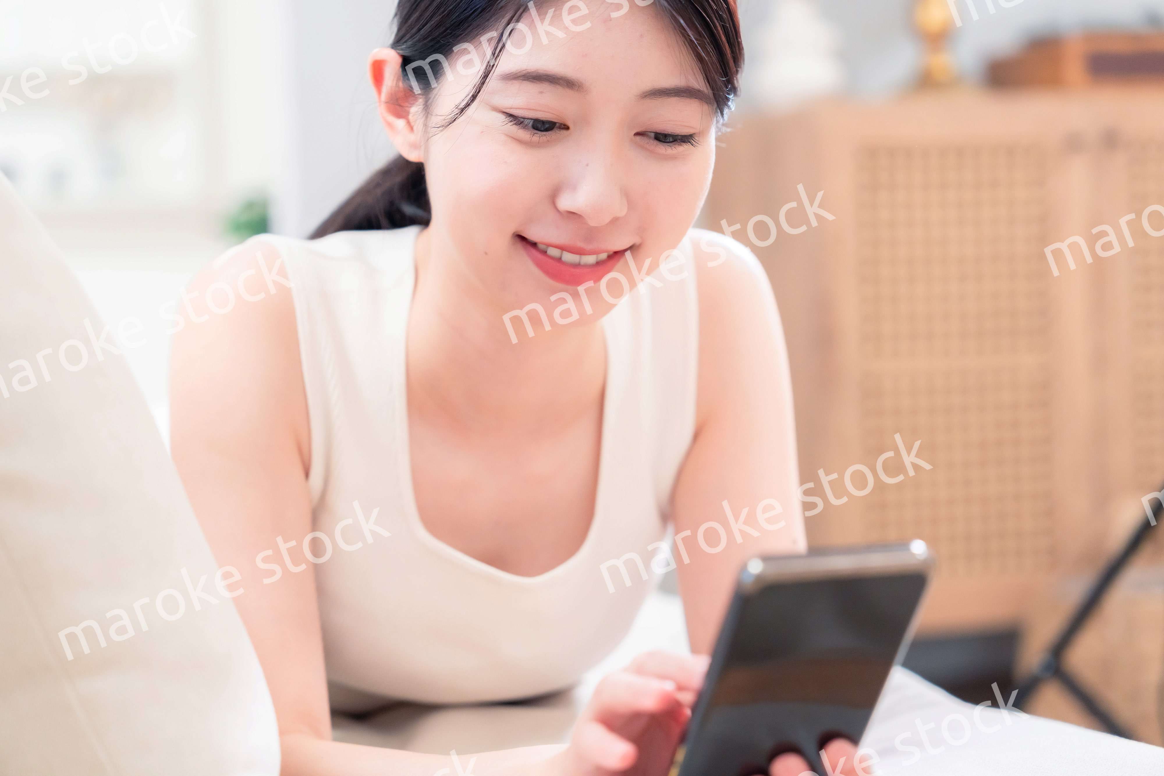 ソファで寝転がってスマホを使う若い女性