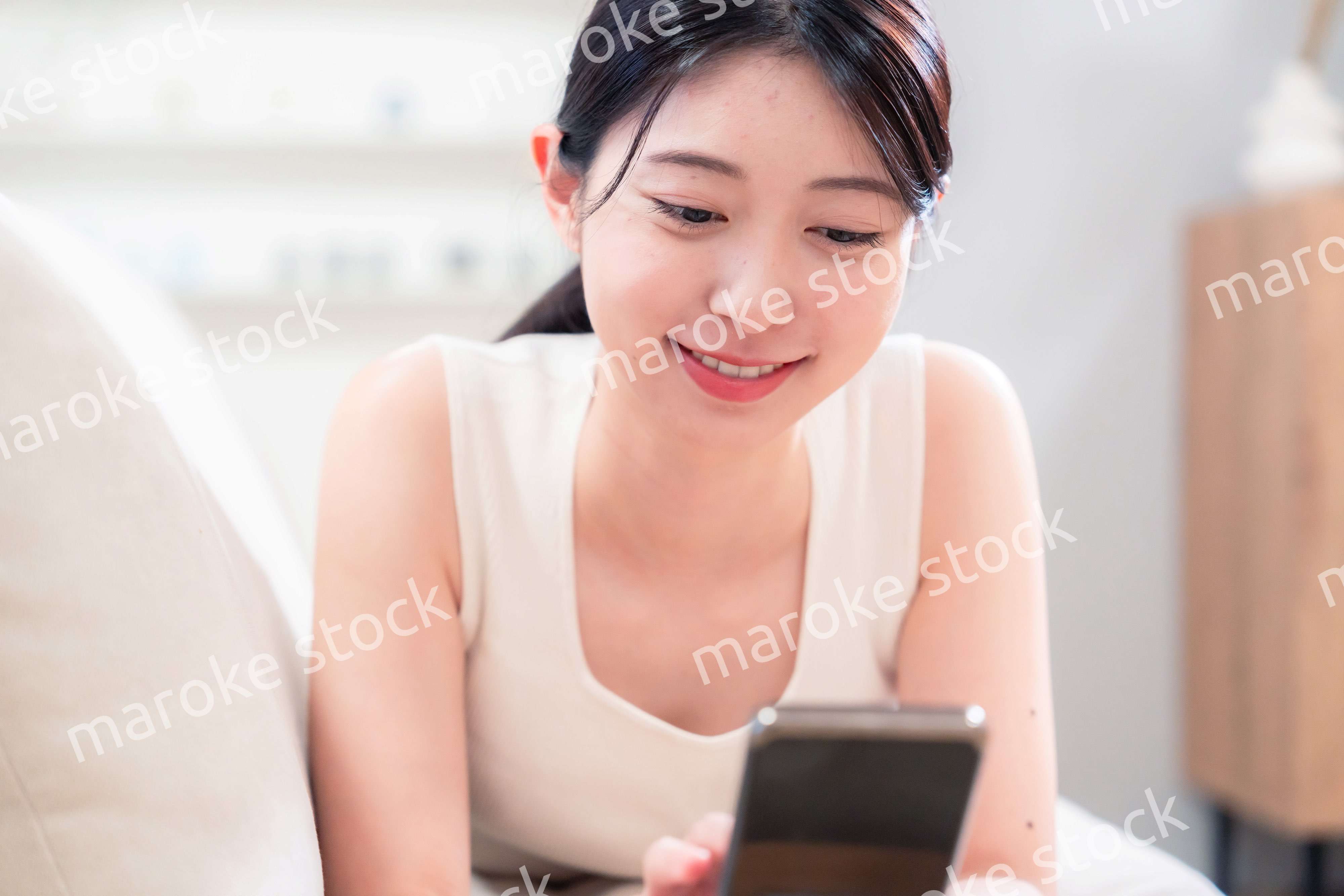ソファで寝転がってスマホを使う若い女性