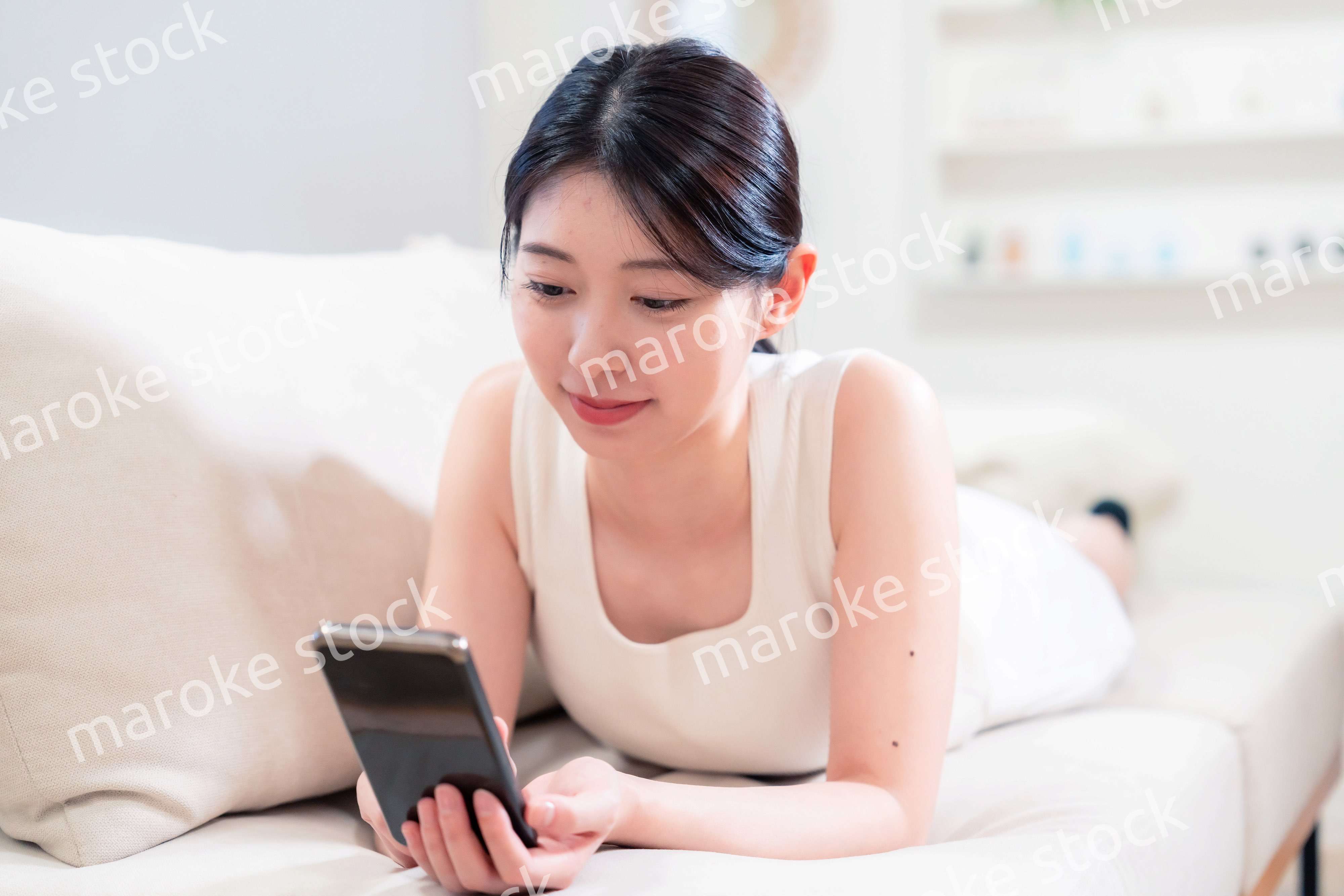 ソファで寝転がってスマホを使う若い女性