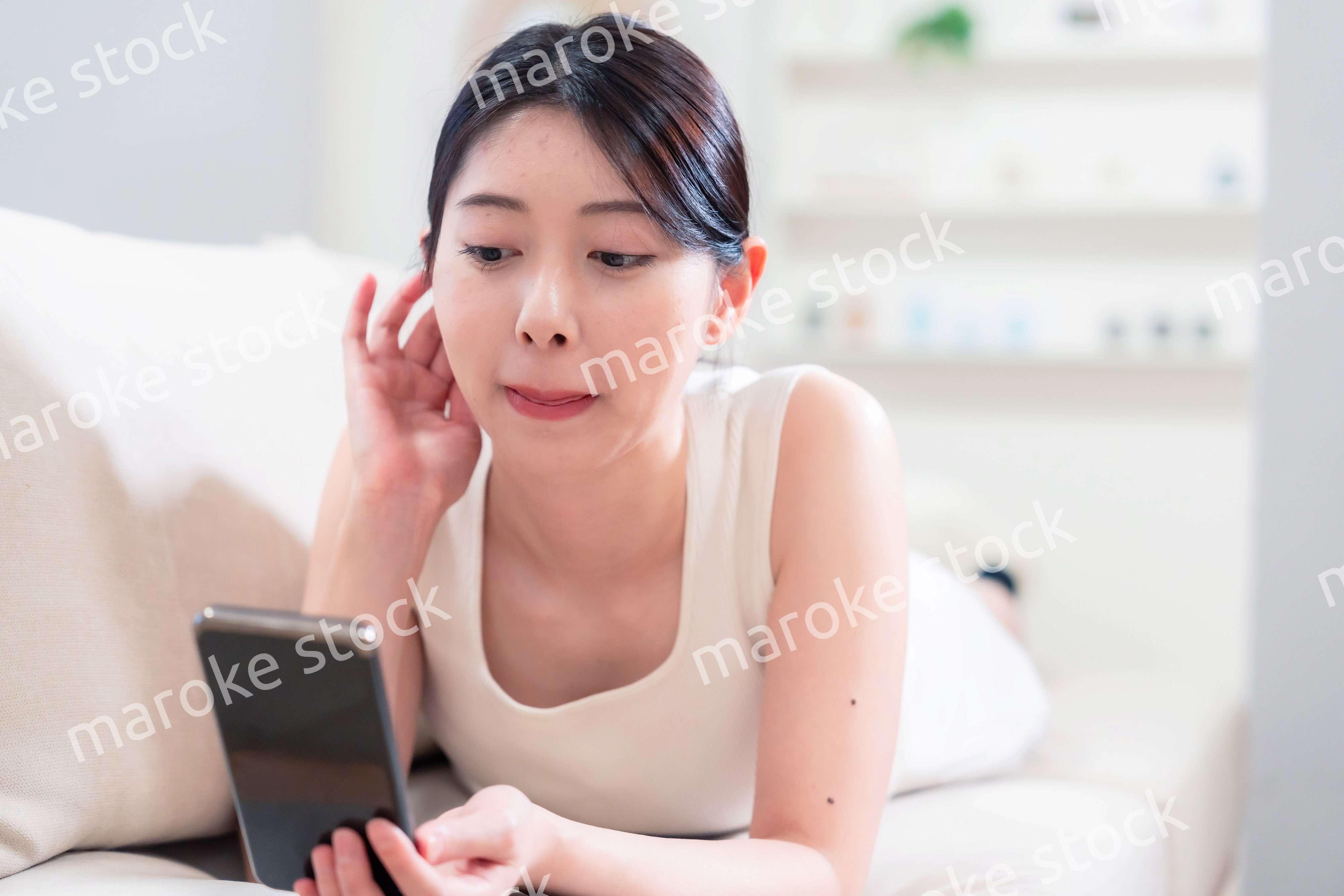 ソファで寝転がってスマホを使う若い女性