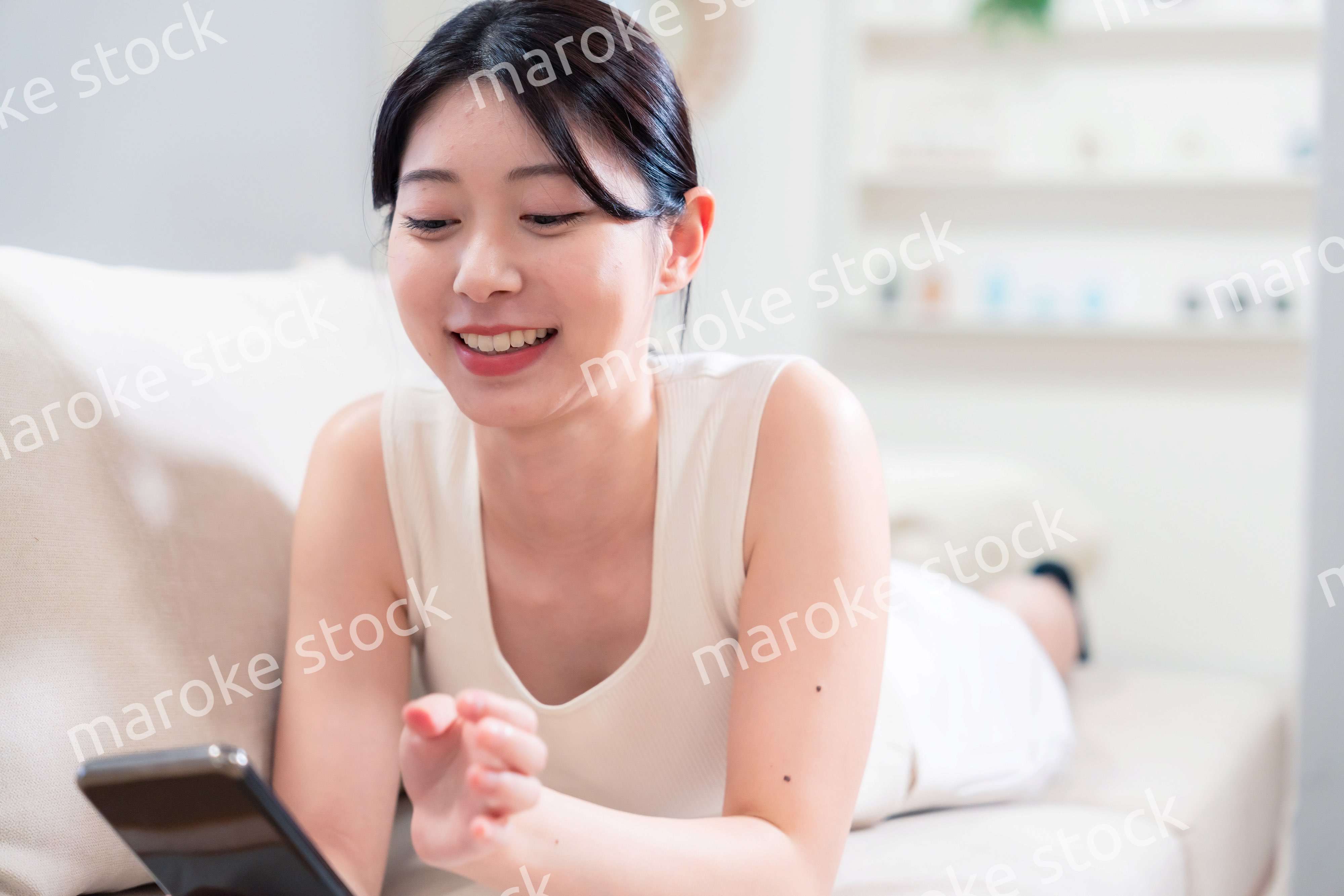 ソファで寝転がってスマホを使う若い女性