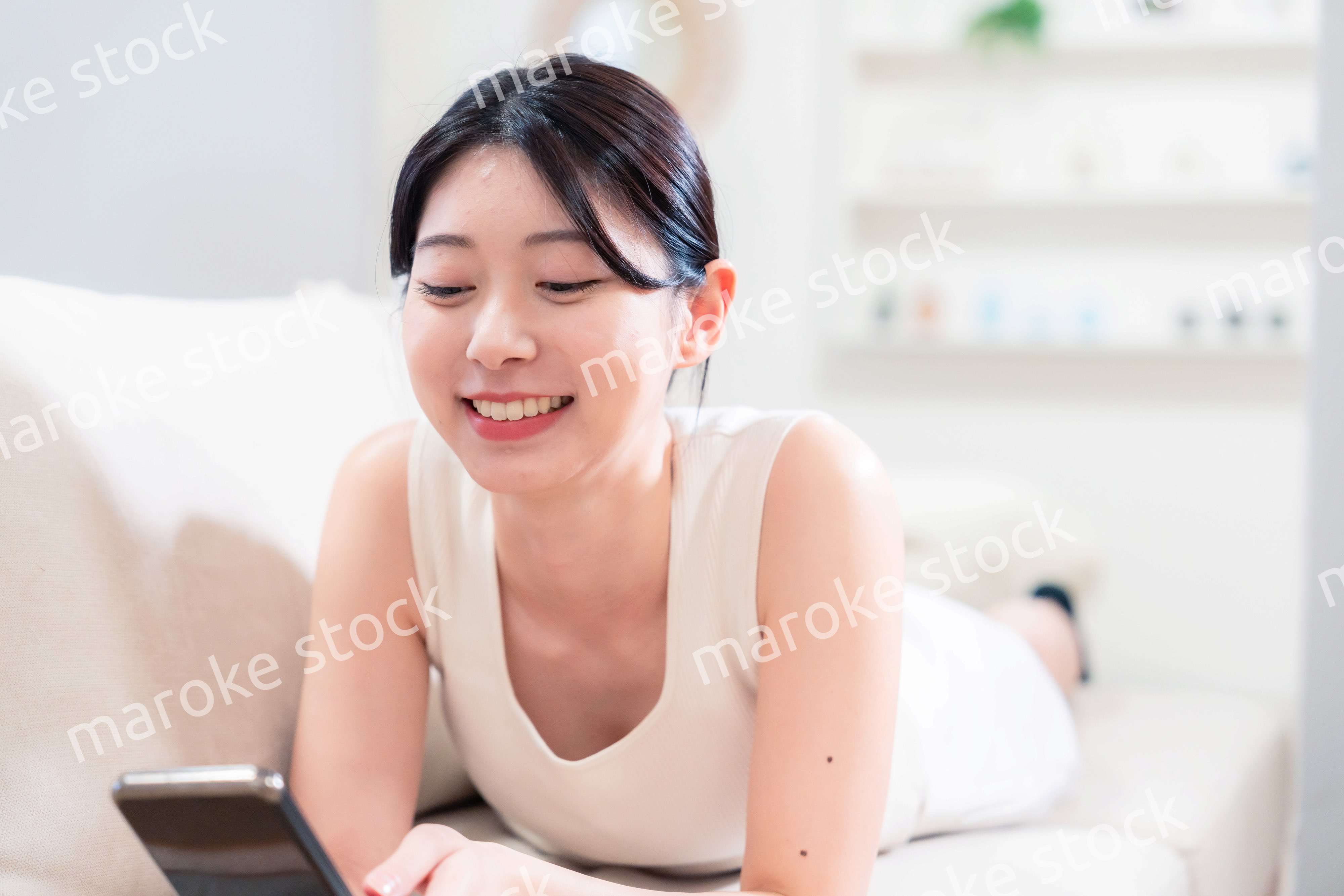 ソファで寝転がってスマホを使う若い女性