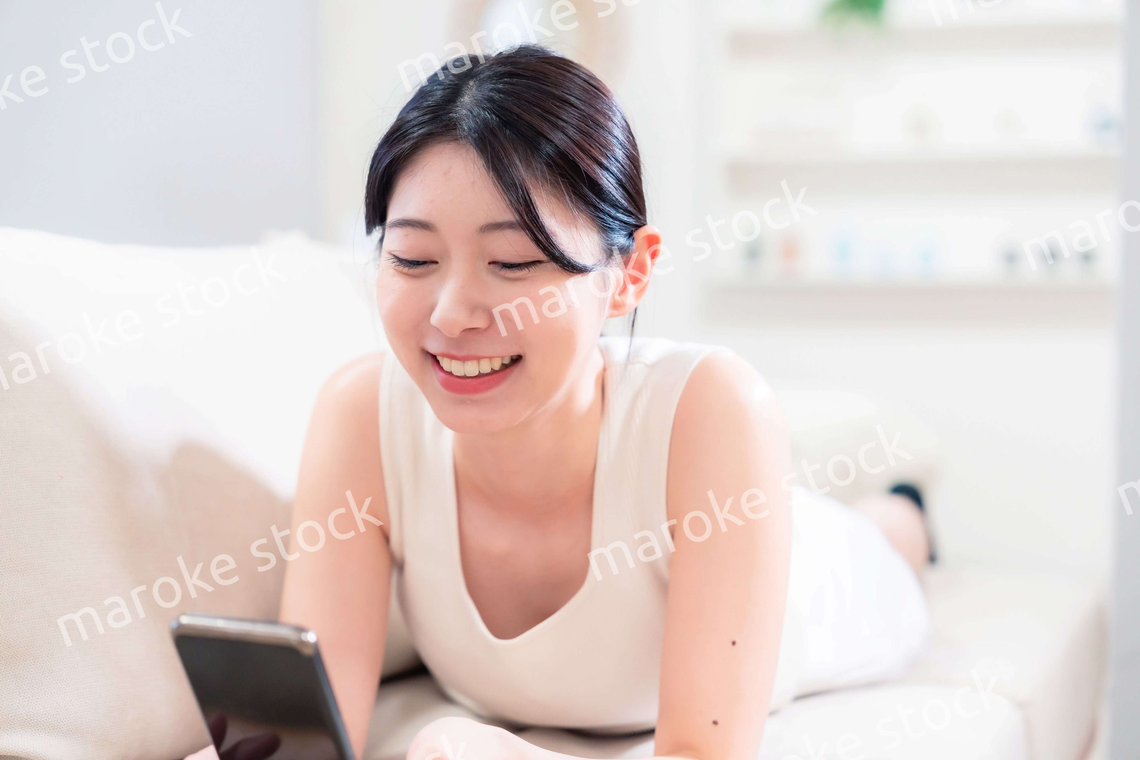ソファで寝転がってスマホを使う若い女性
