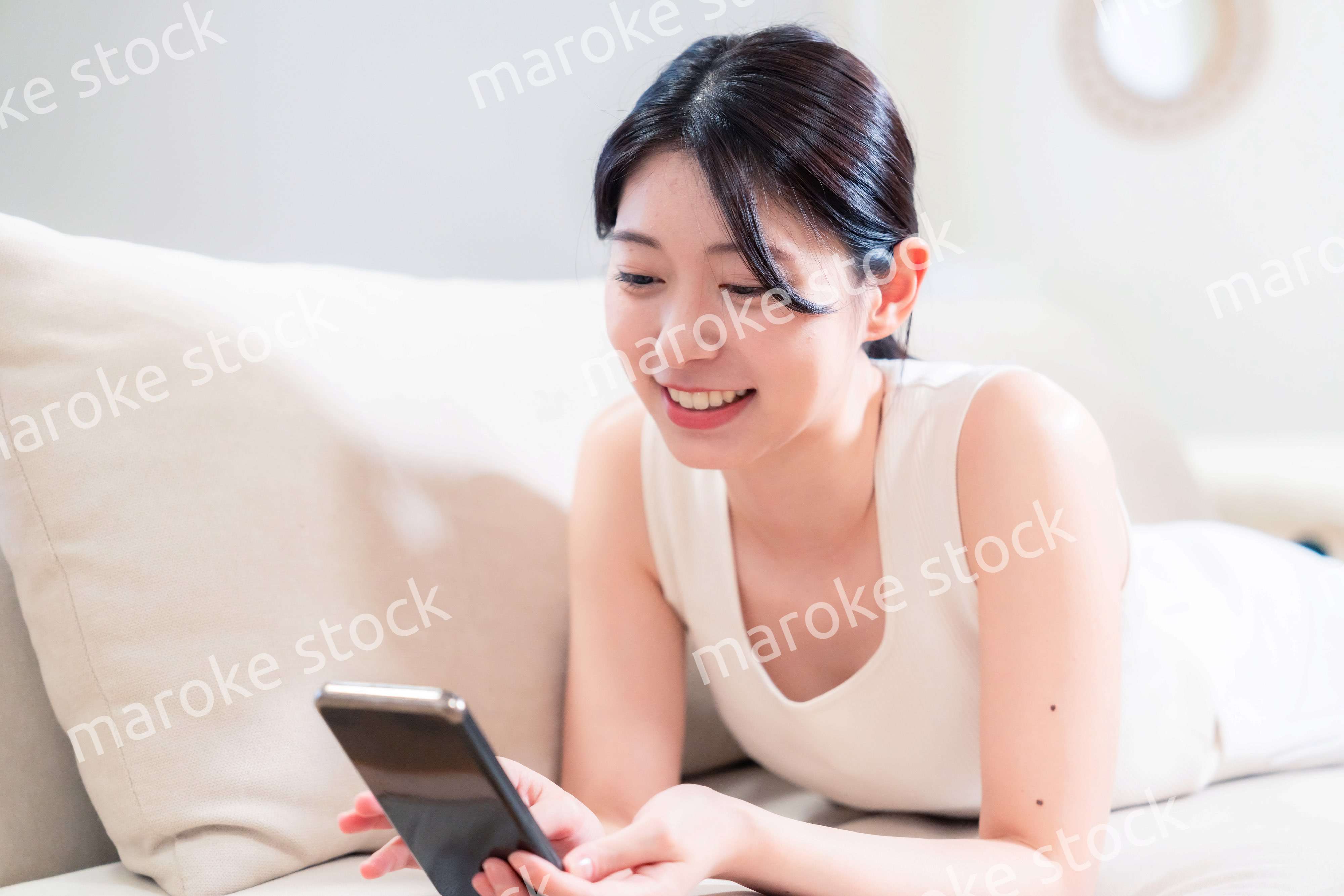 ソファで寝転がってスマホを使う若い女性