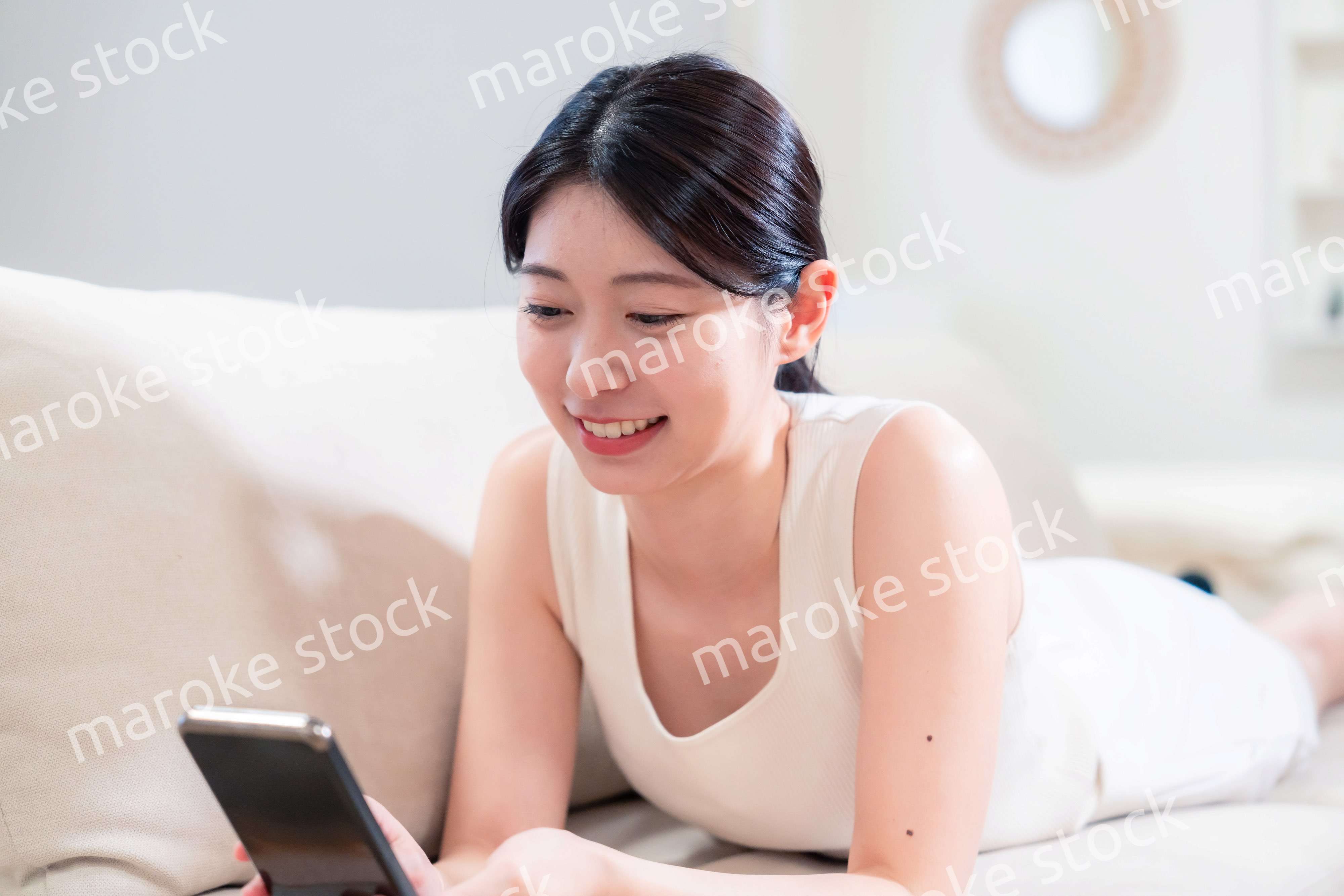 ソファで寝転がってスマホを使う若い女性