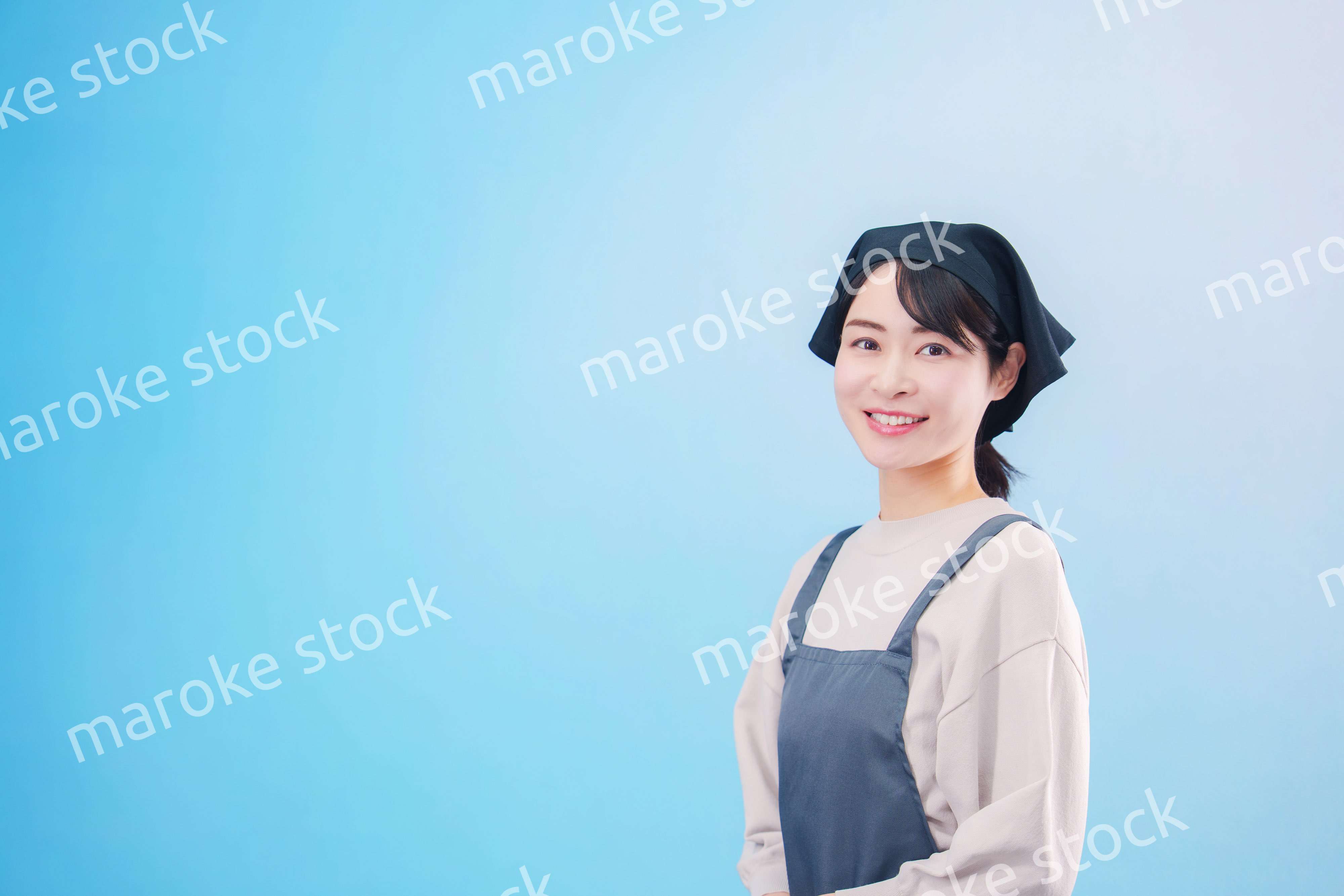エプロンを着た調理師の若い女性（水色背景）