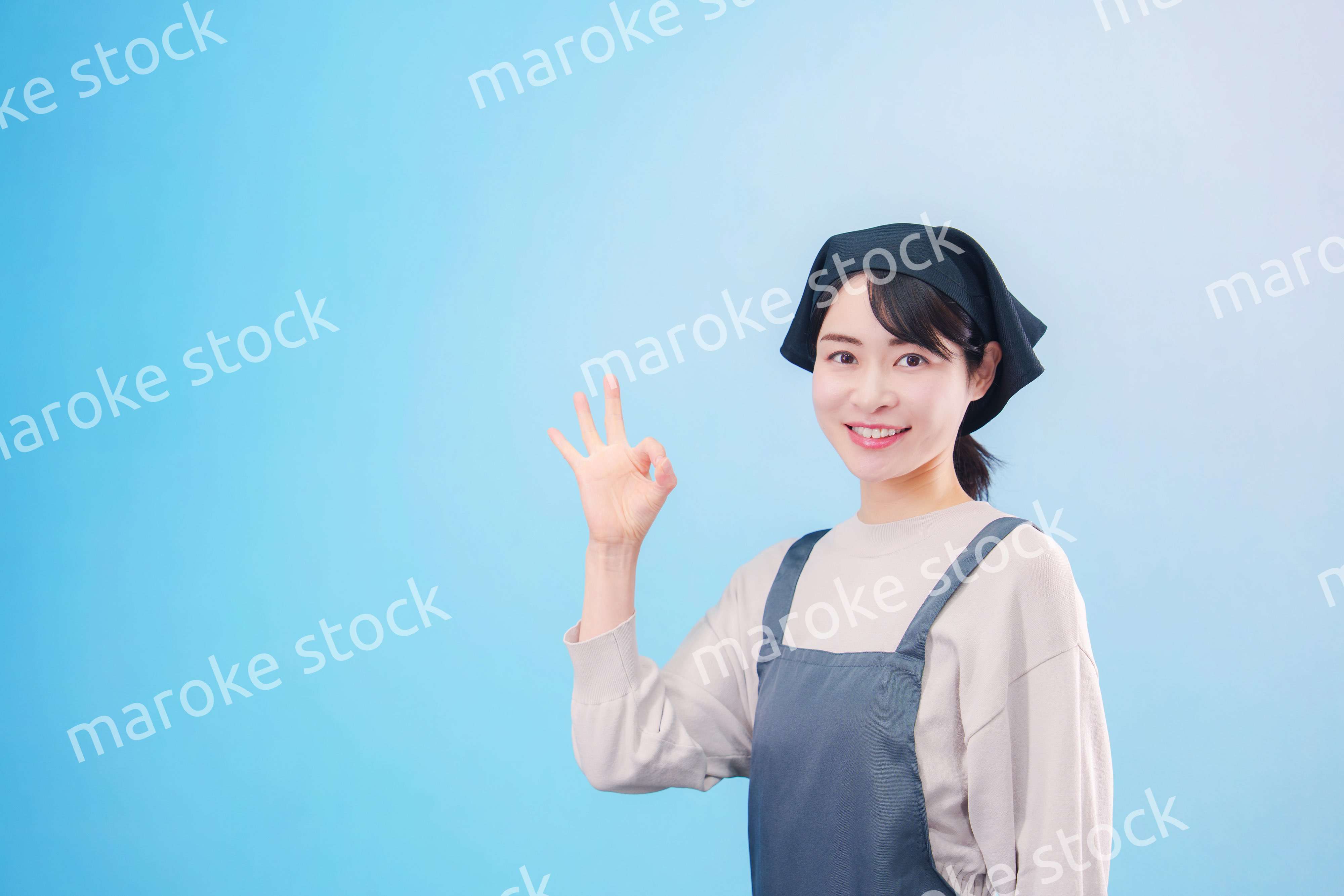 エプロンを着た調理師の若い女性（水色背景）