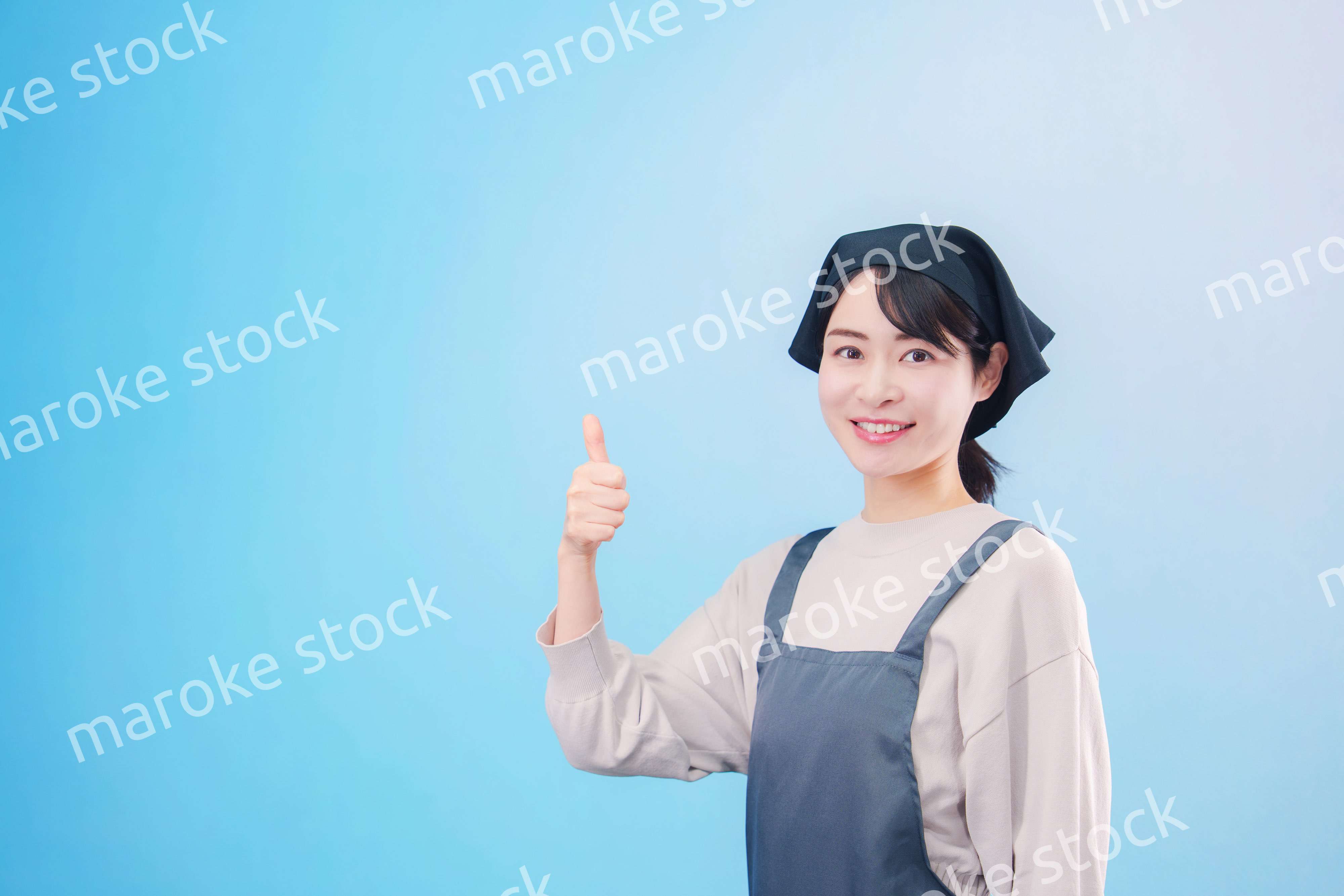 エプロンを着た調理師の若い女性（水色背景）