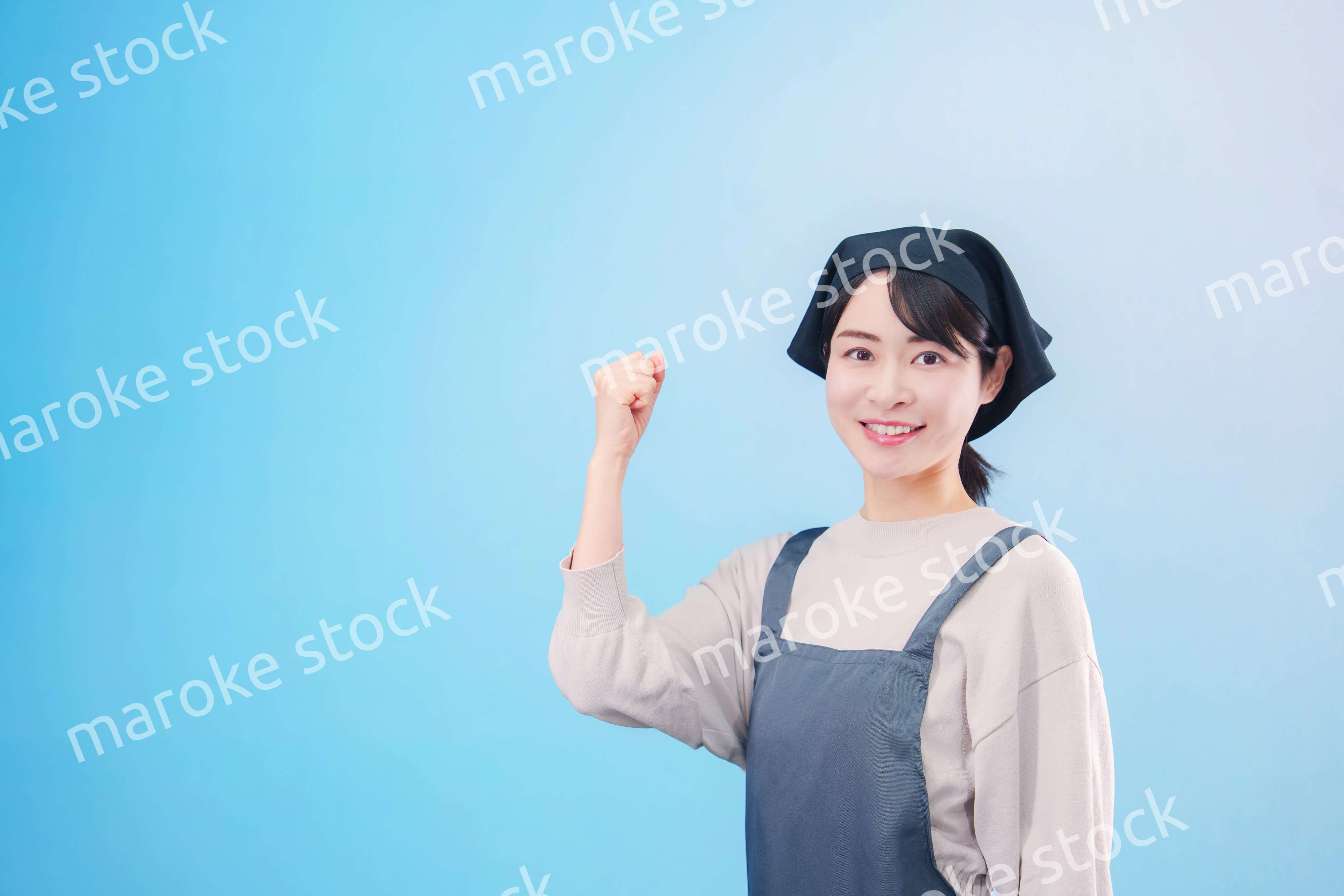 エプロンを着た調理師の若い女性（水色背景）