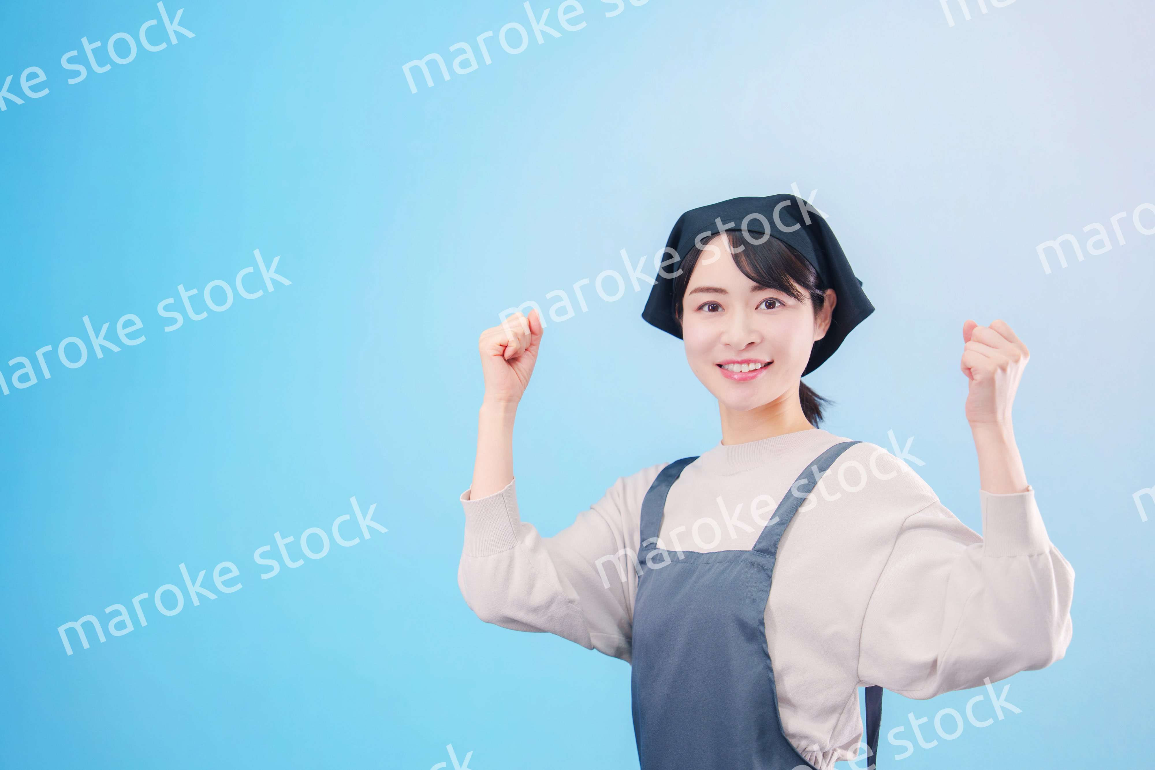 エプロンを着た調理師の若い女性（水色背景）