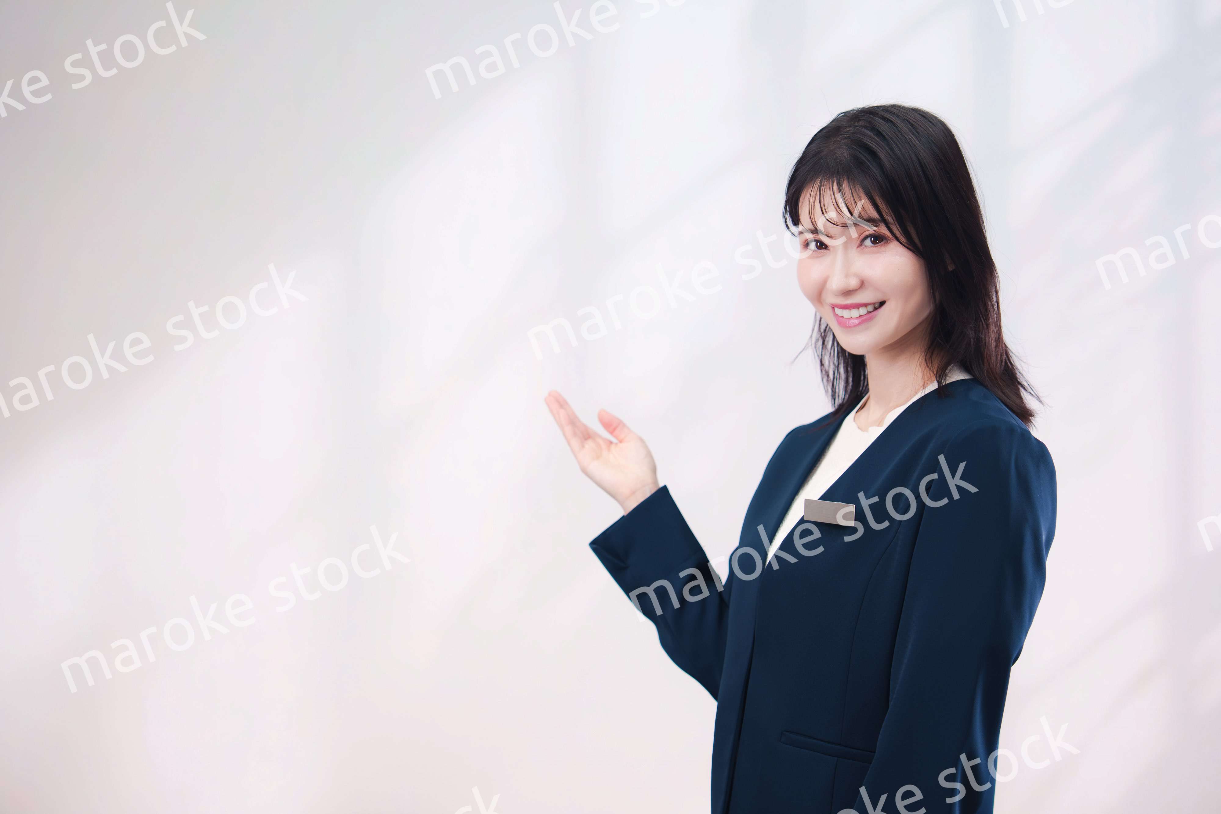 名札をつけて笑顔で接客をする若い女性（シンプル背景）
