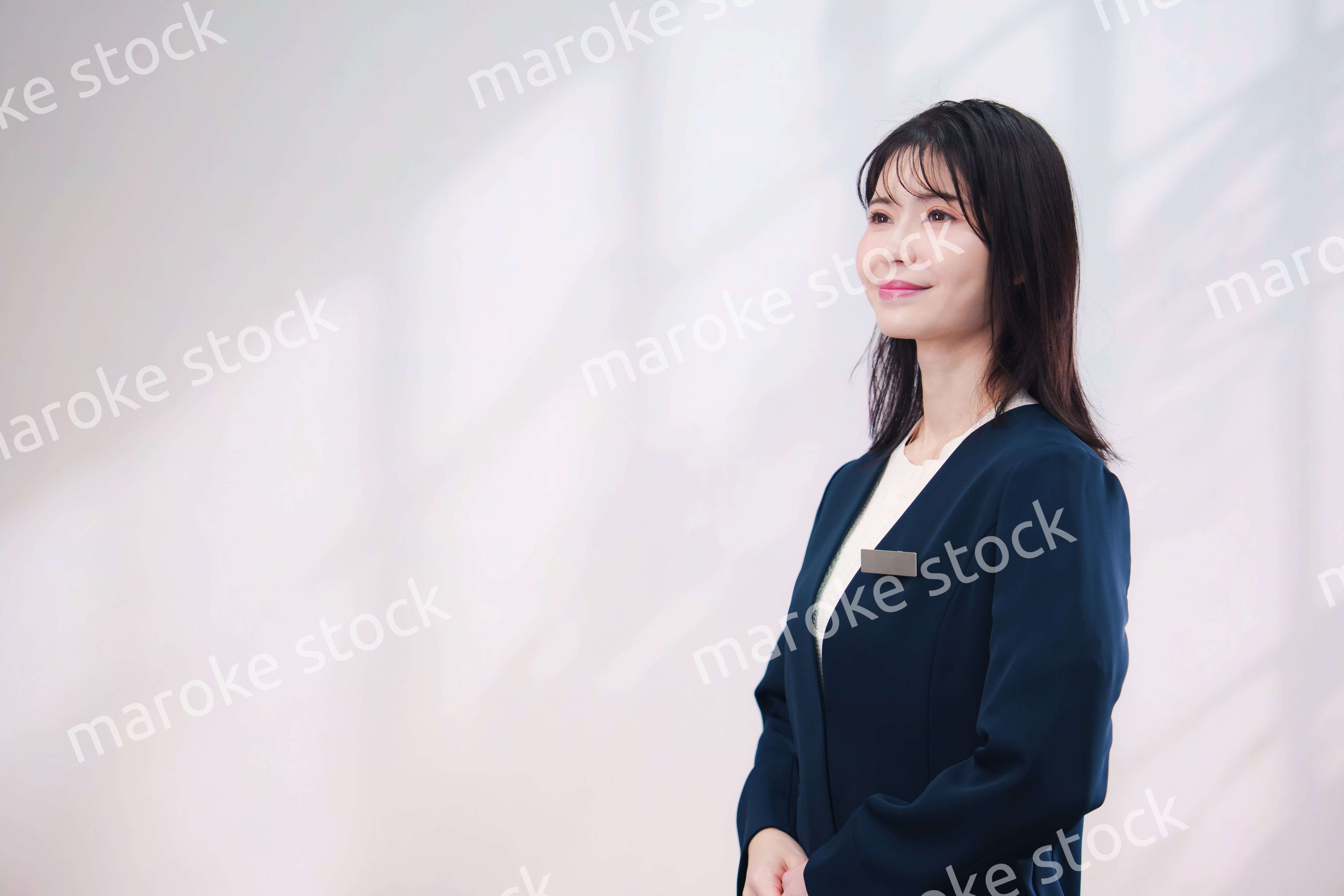 名札をつけて笑顔で接客をする若い女性（シンプル背景）