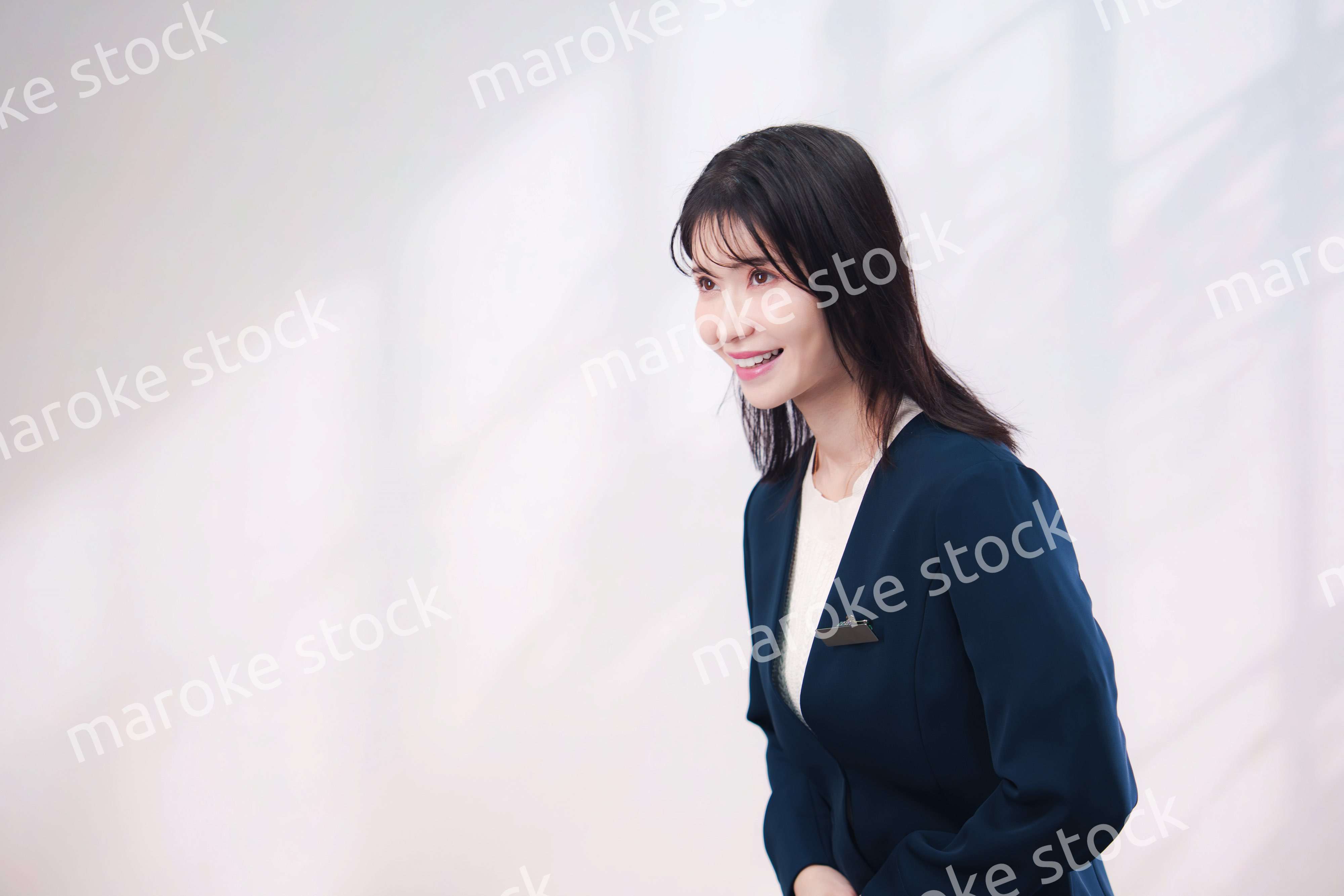 名札をつけて笑顔で接客をする若い女性（シンプル背景）