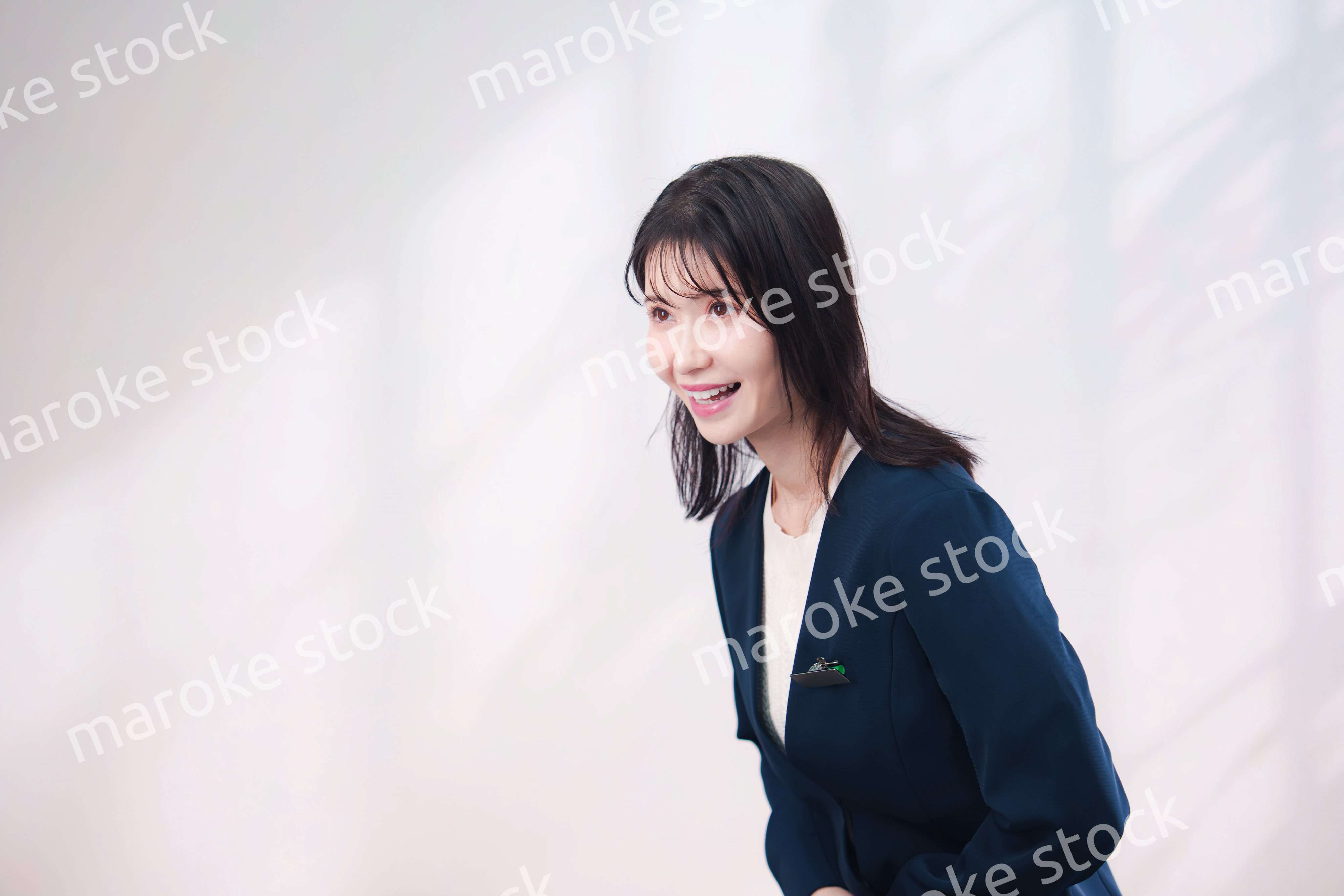 名札をつけて笑顔で接客をする若い女性（シンプル背景）