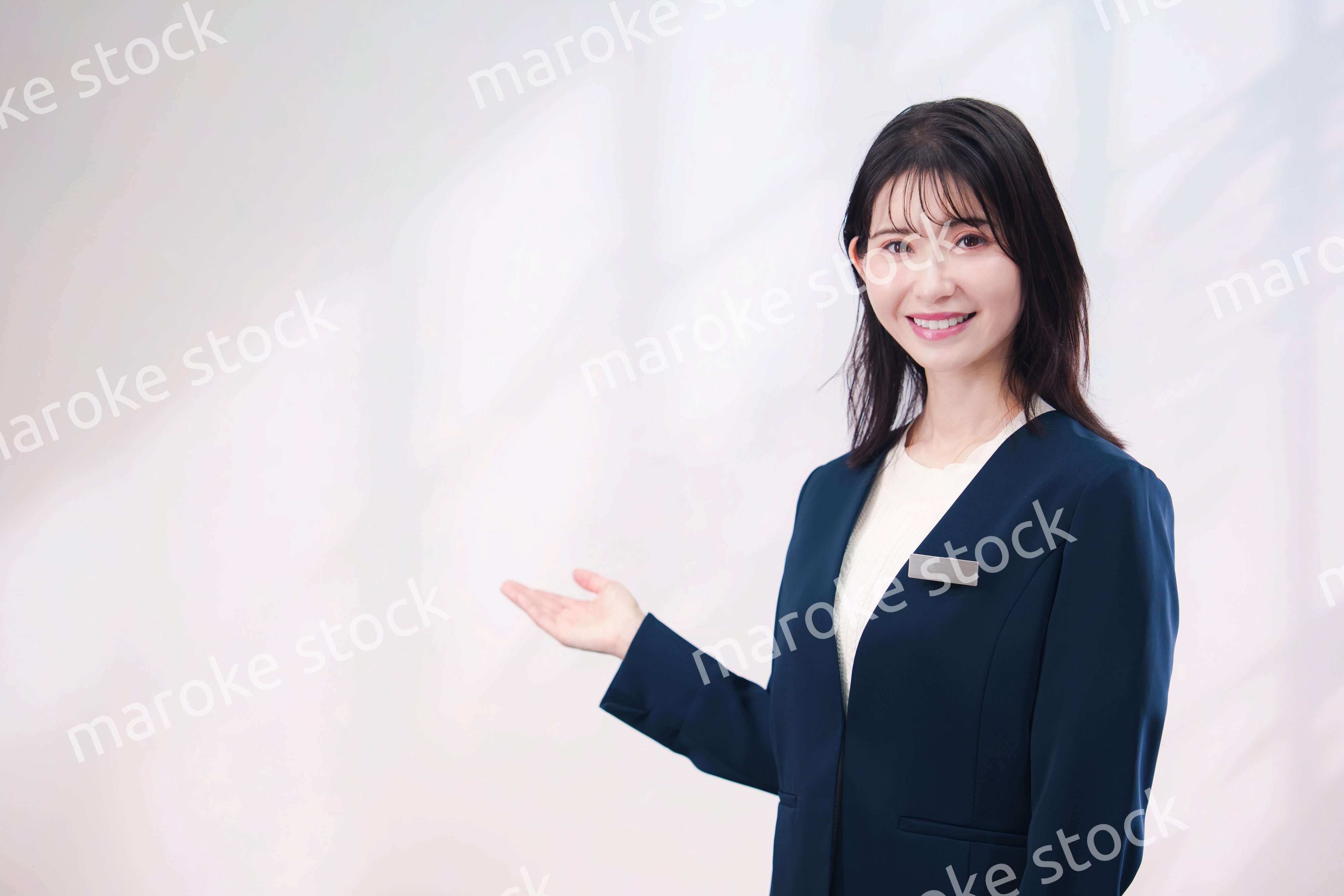 名札をつけて笑顔で接客をする若い女性（シンプル背景）