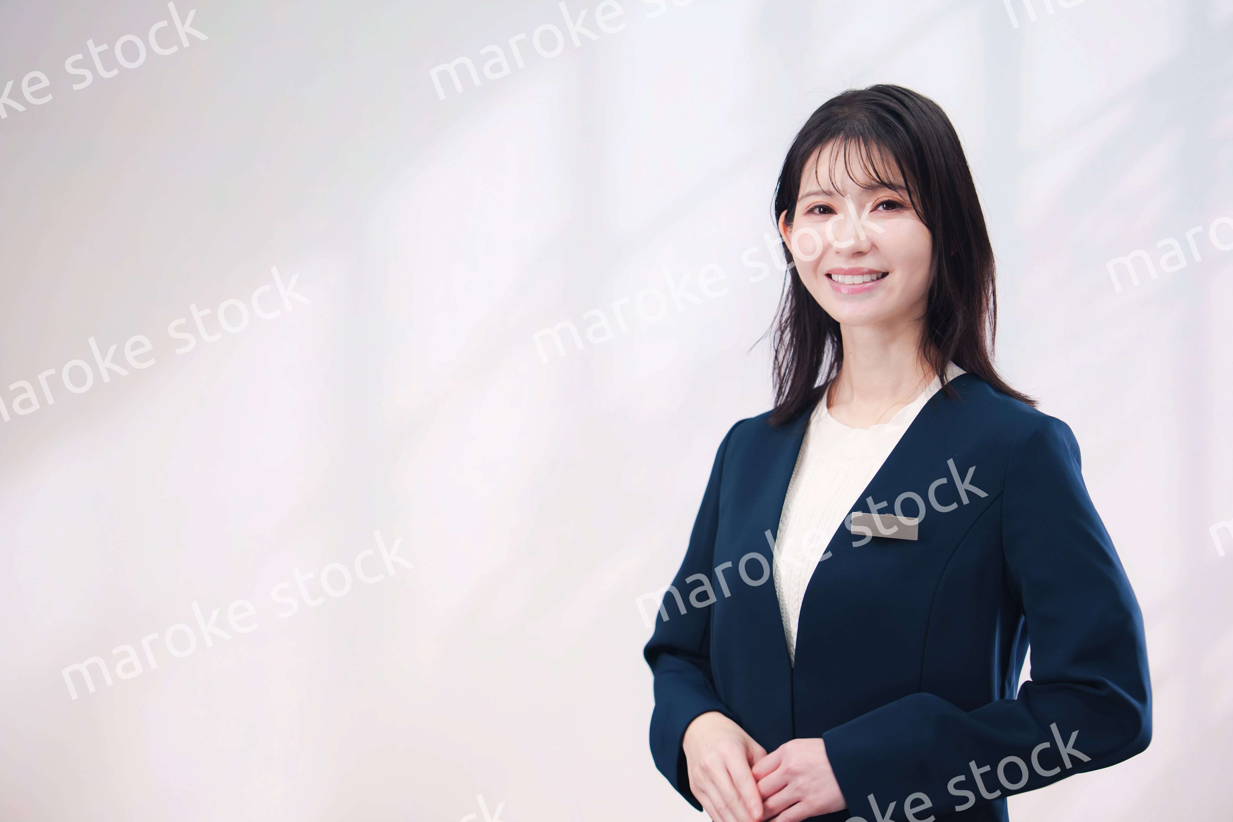 名札をつけて笑顔で接客をする若い女性（シンプル背景）