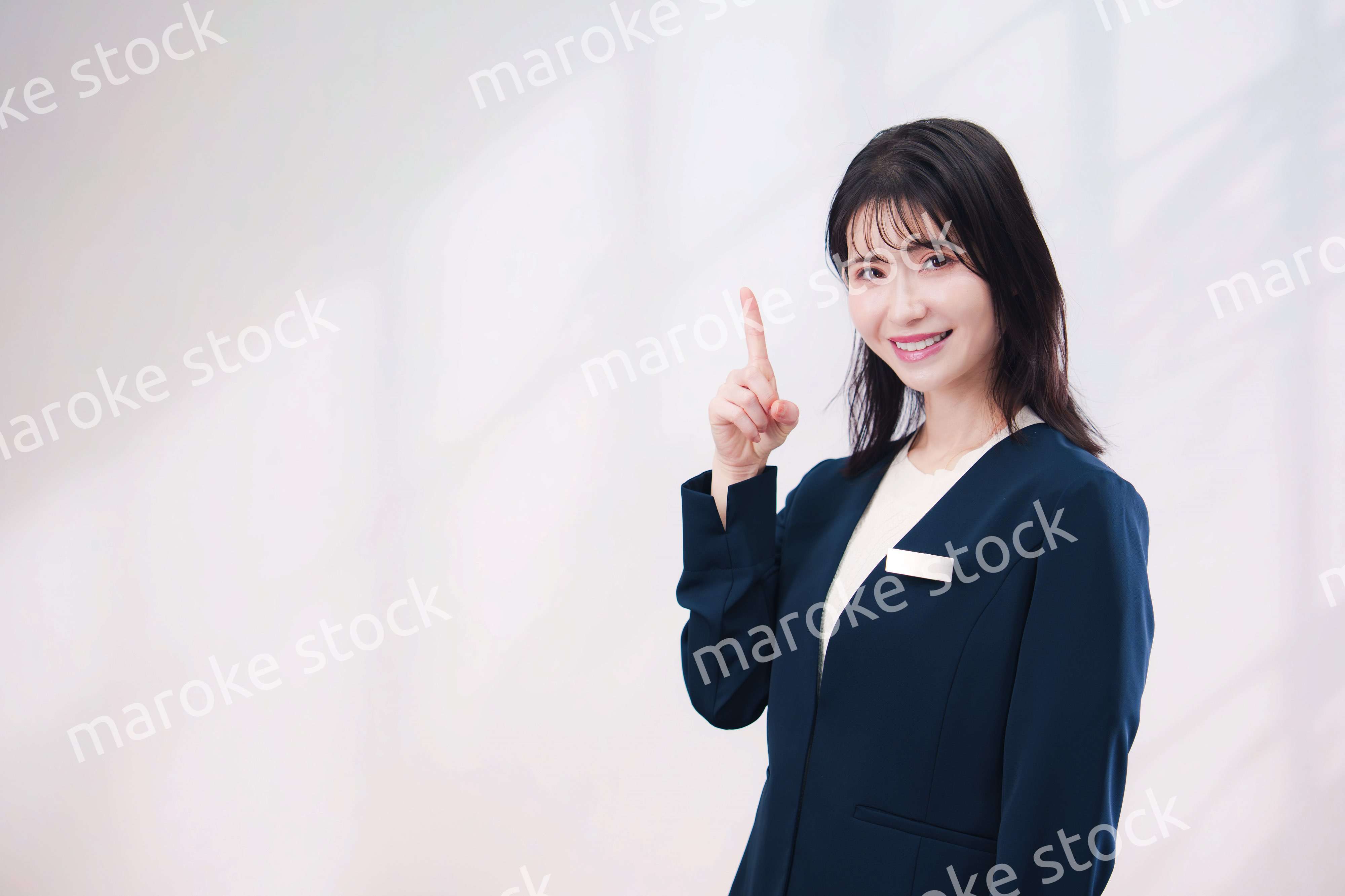 名札をつけて笑顔で接客をする若い女性（シンプル背景）