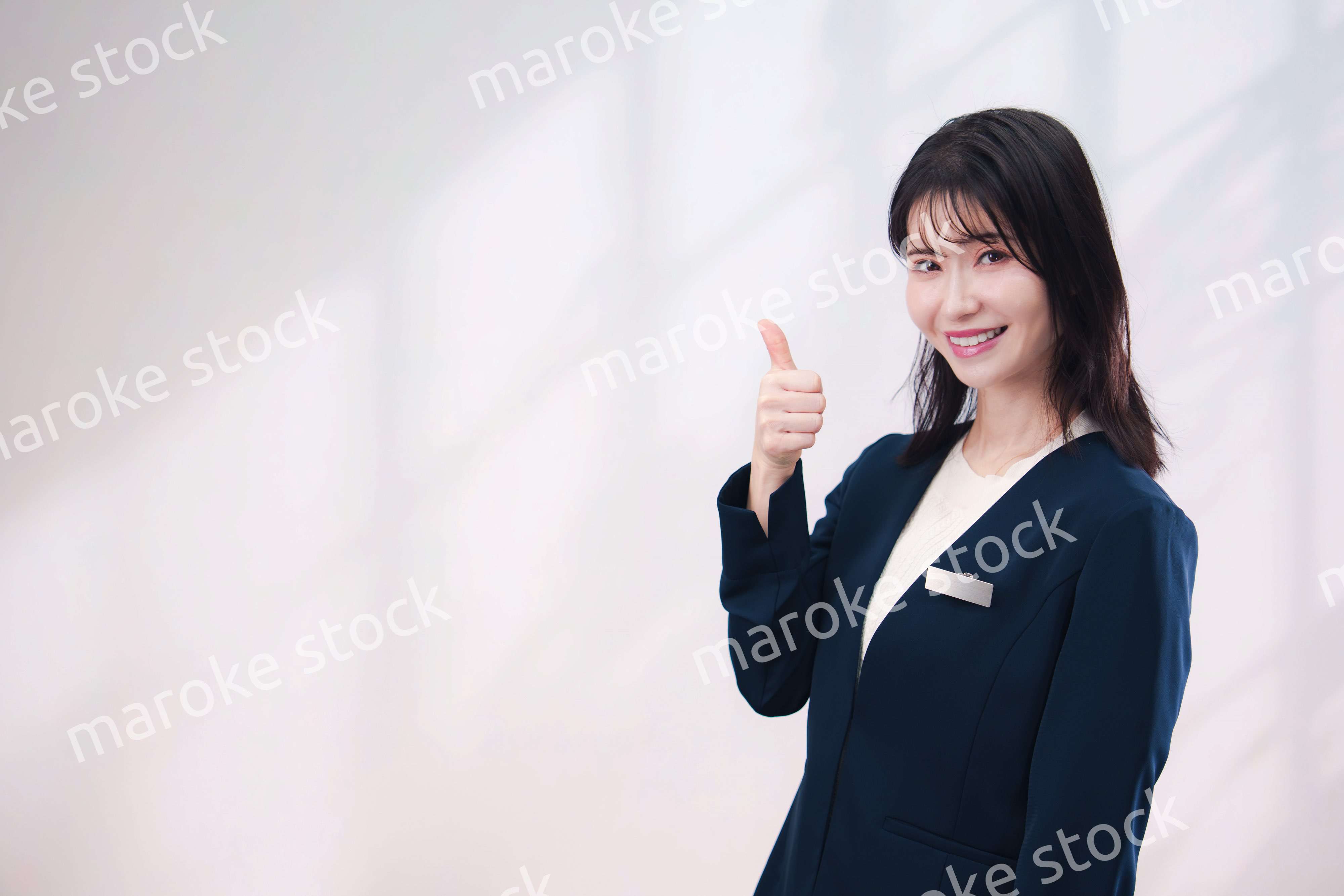 名札をつけて笑顔で接客をする若い女性（シンプル背景）