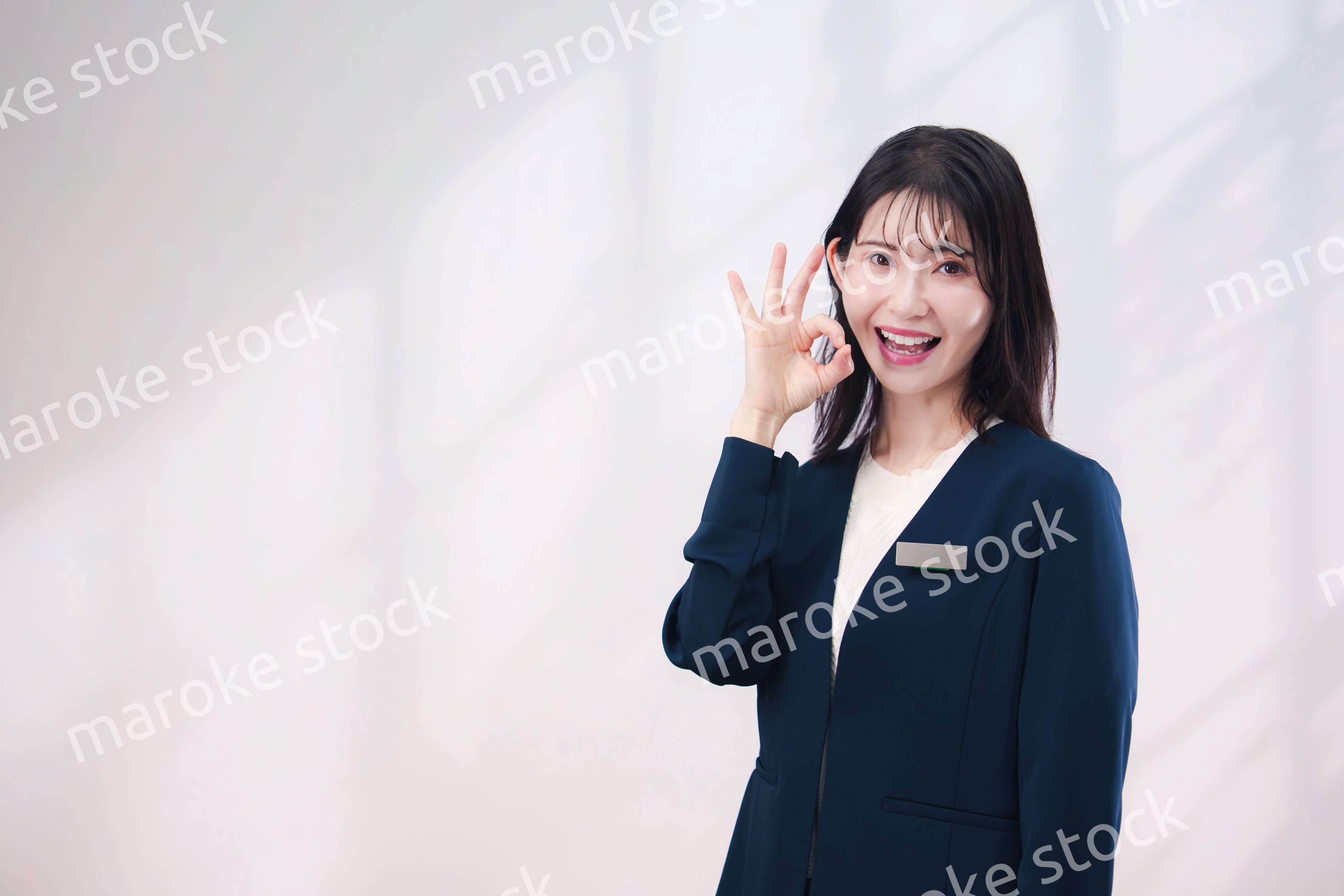 名札をつけて笑顔で接客をする若い女性（シンプル背景）