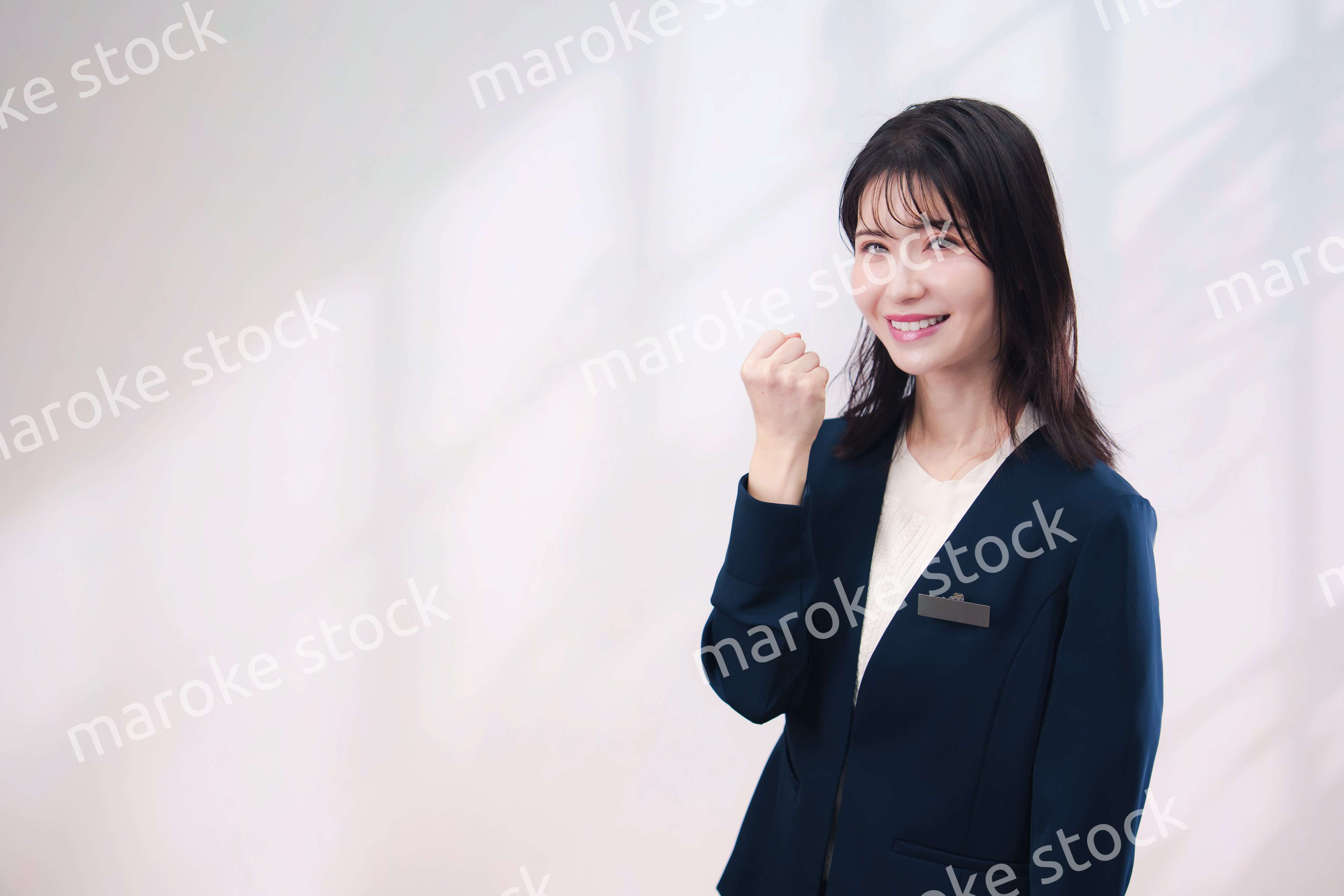 名札をつけて笑顔で接客をする若い女性（シンプル背景）