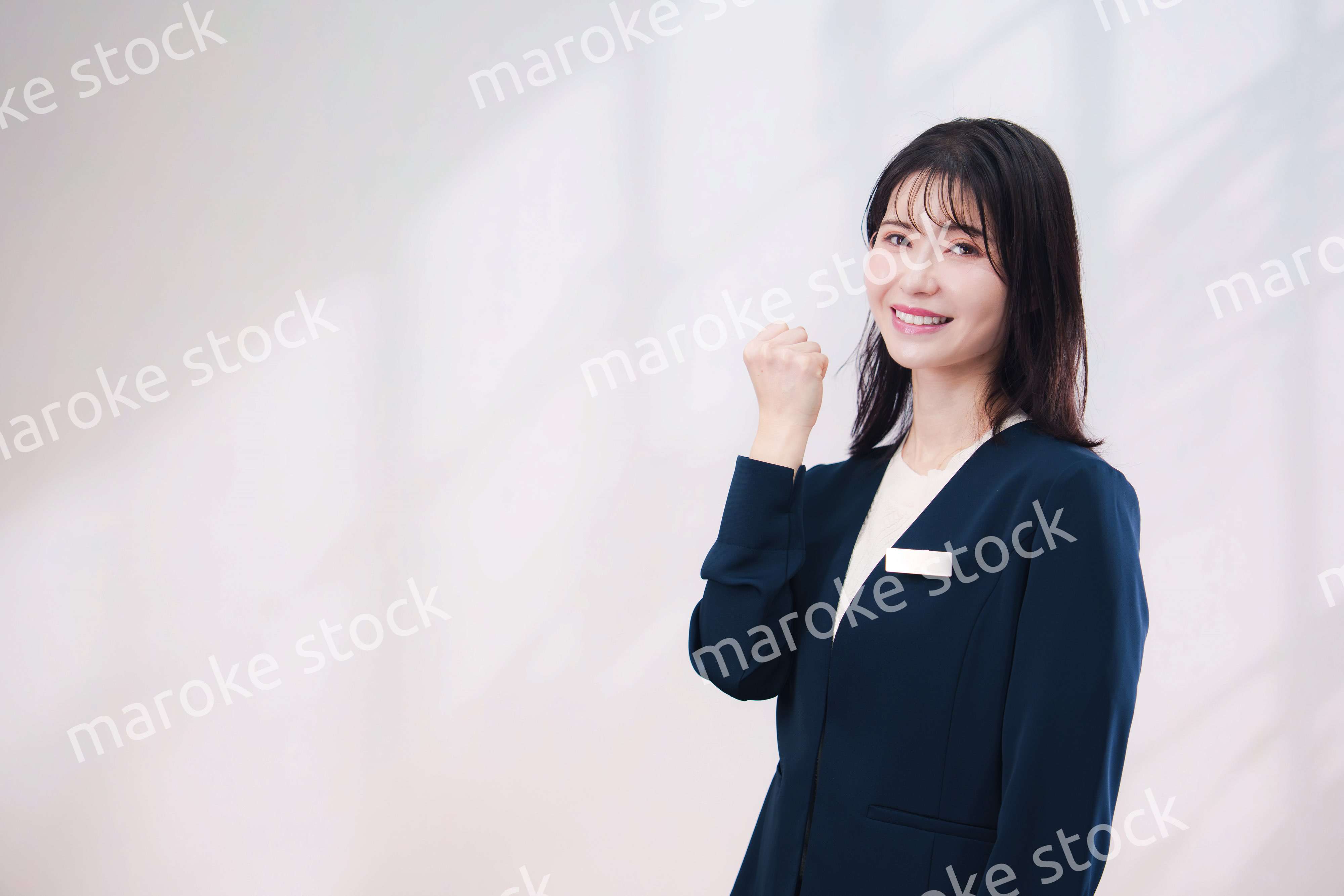 名札をつけて笑顔で接客をする若い女性（シンプル背景）